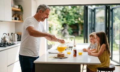 Grandfather laughing with grandchildren over breakfast in a sunlit modern kitchen