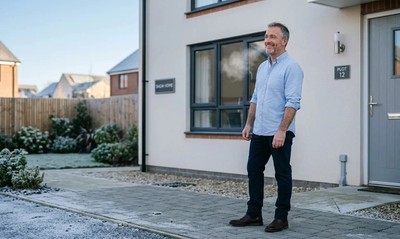 Man in rolled-sleeve shirt stands relieved outside a new-build show home on a winter morning