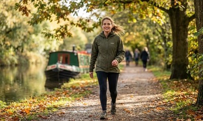 Woman walking along a sunlit canal towpath on a bright autumn morning