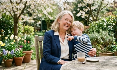 A woman in a suit shares a warm laugh with her grandchild on a sunlit spring patio