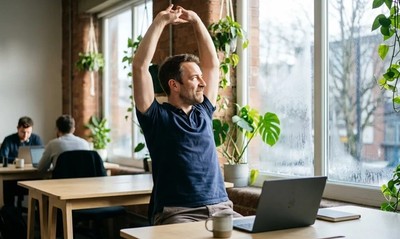 Man in polo shirt stretching by a bright window in a modern co-working space on a winter morning