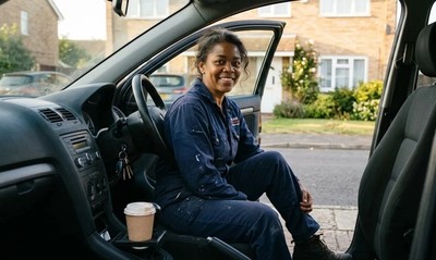 Woman in work overalls sits in her car outside her new home after porting her mortgage