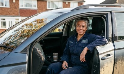 Self-employed tradeswoman in overalls sits in her car outside her home, considering a freelancer mortgage.