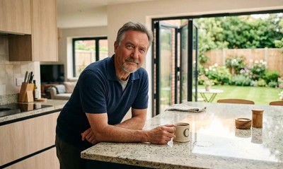 Man in his late fifties in a sunlit new-build kitchen, thinking about his mortgage overpayments