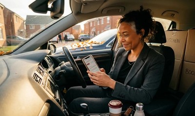 Woman in car outside new-build home checking mortgage offer email on moving day