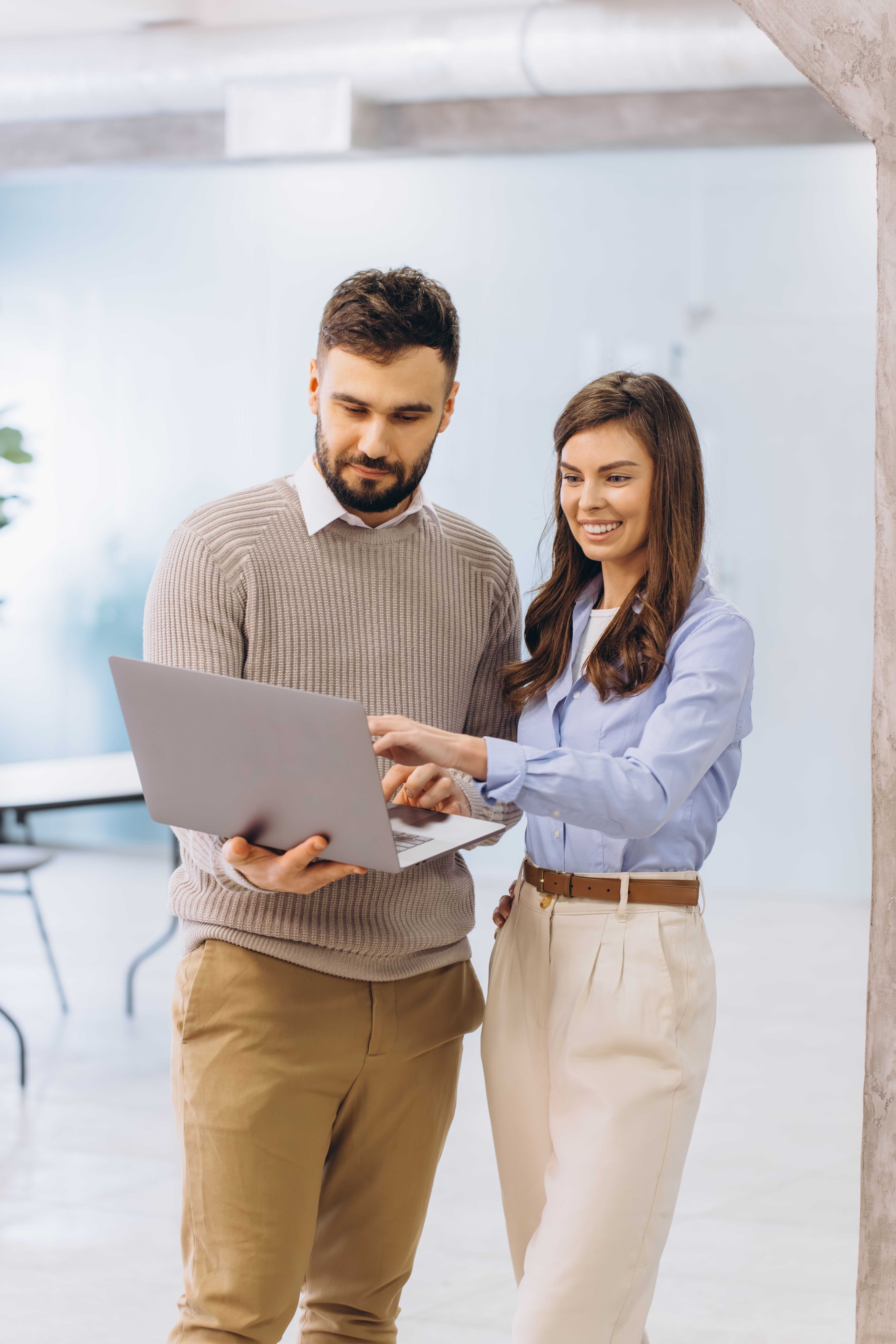 Two business colleagues standing, using a laptop, pointing at screen and discussing work. Team workin