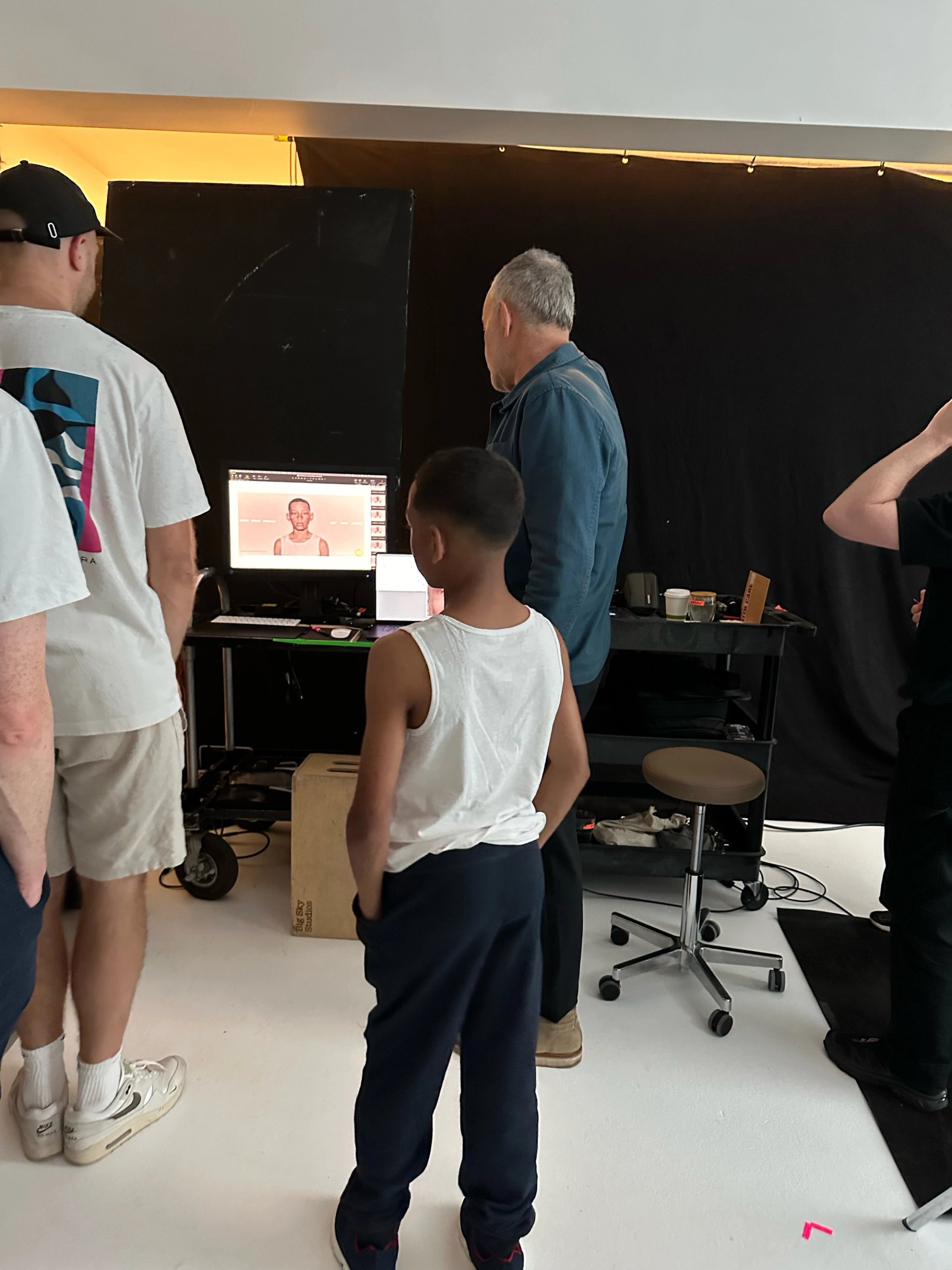 Young boy in white vest and crew reviewing portrait on monitor in photo studio behind the scenes of YES! campaign