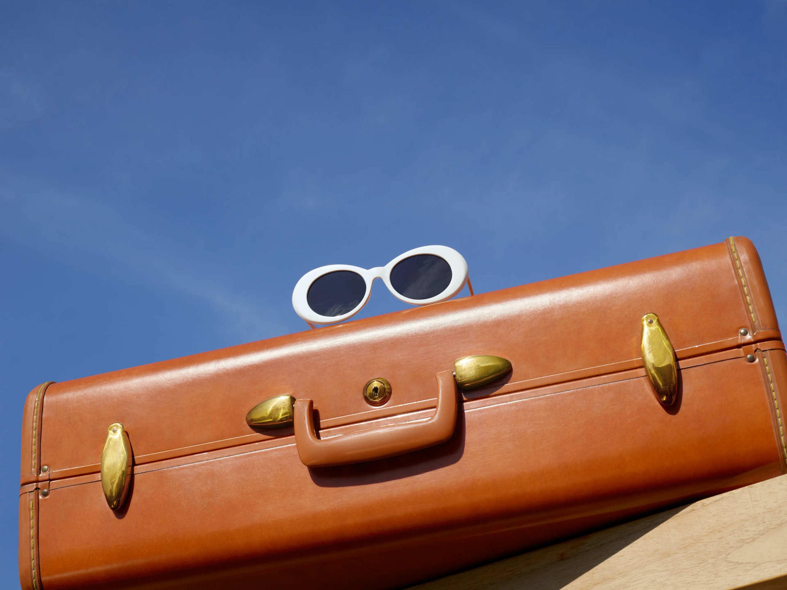 Tan leather vintage suitcase with white round sunglasses against blue sky for Hoxton Hotel Dis-Loyalty campaign