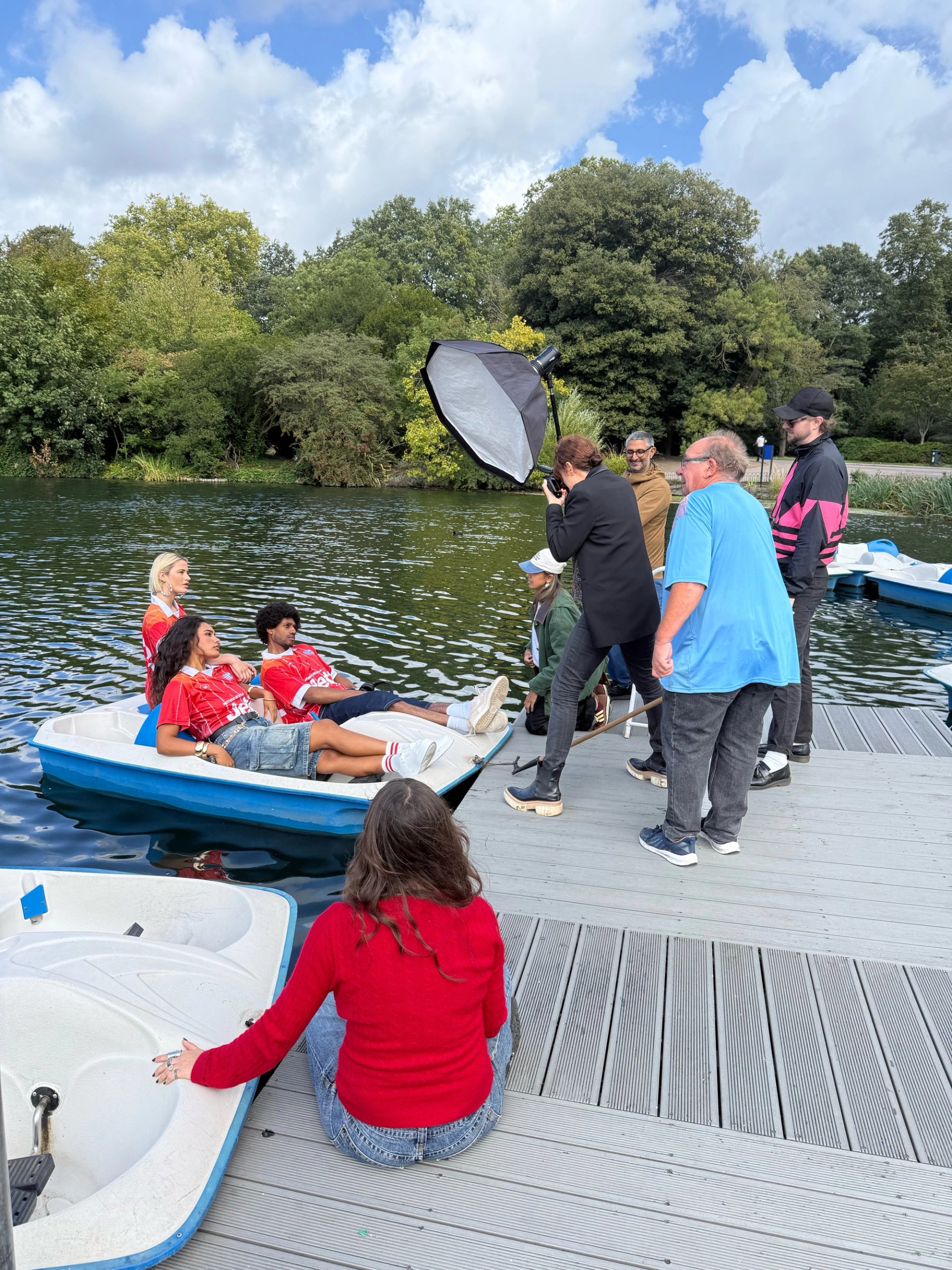 Behind the scenes of Jet2 shoot with crew on lake jetty photographing models in red jerseys in pedal boat with softbox
