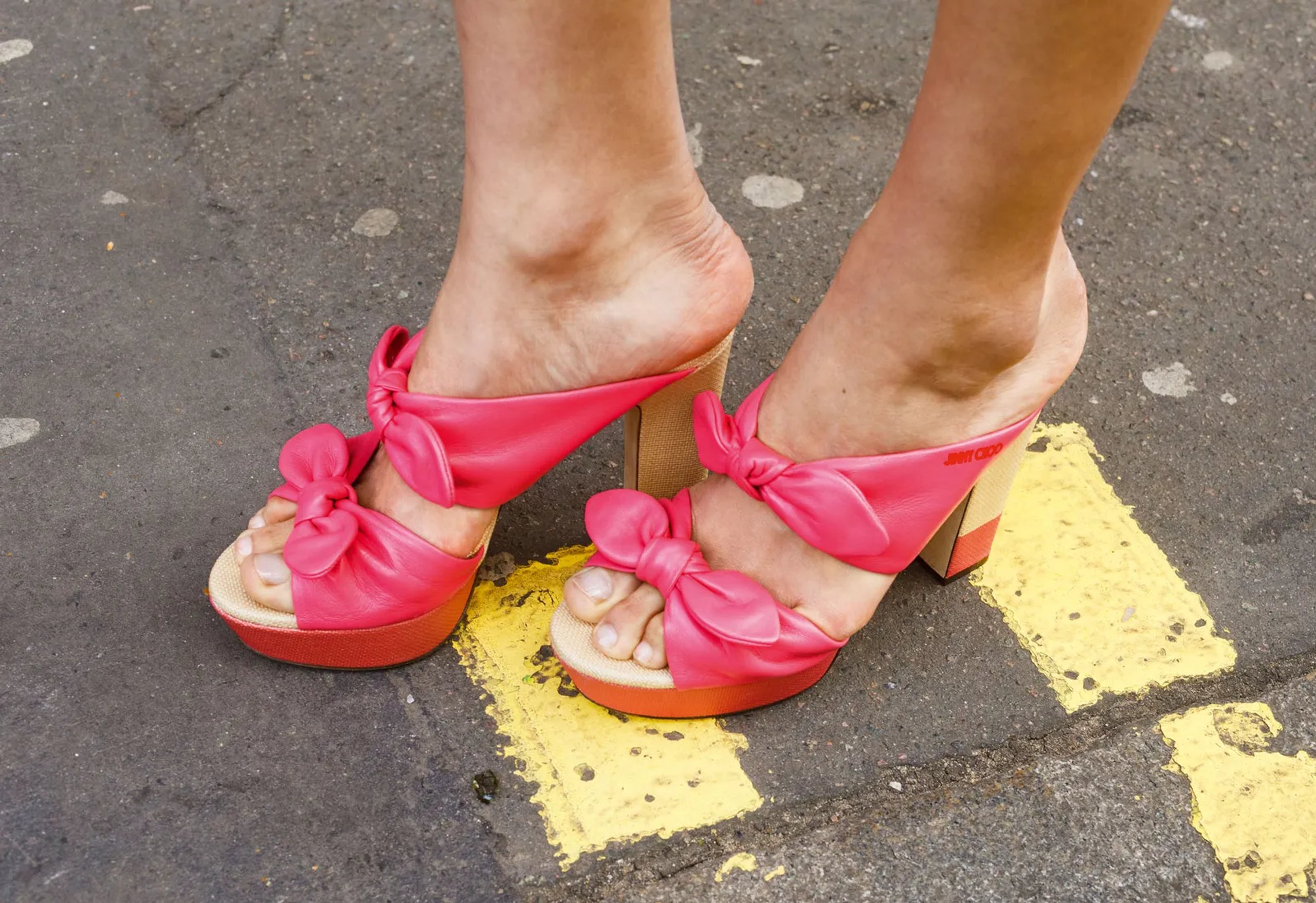 Close-up of pink knotted bow platform mules on London street tarmac