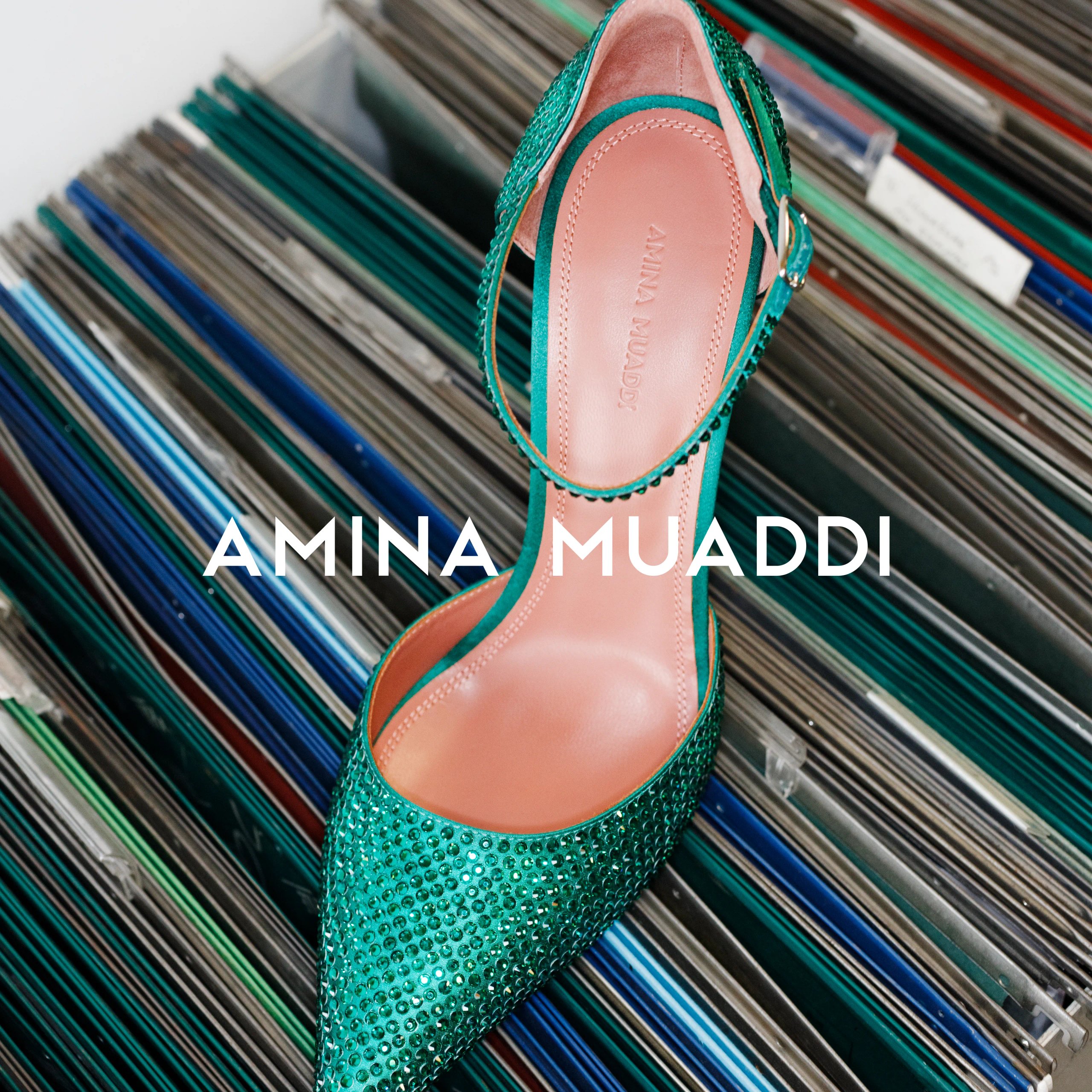 Amina Muaddi emerald green crystal pump on stack of vinyl records