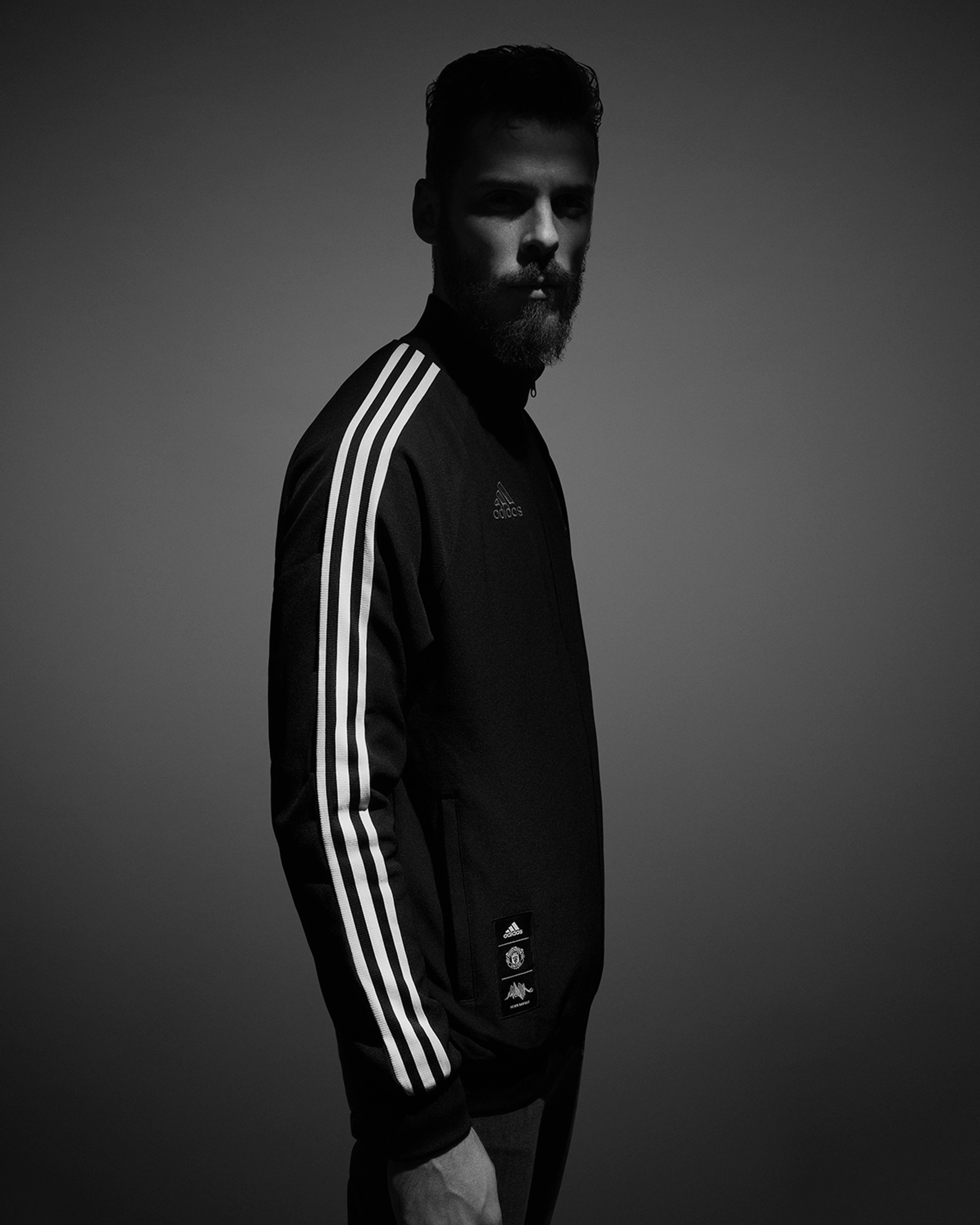 Black and white profile portrait in adidas x Manchester United Peter Saville track top with three-stripe sleeve