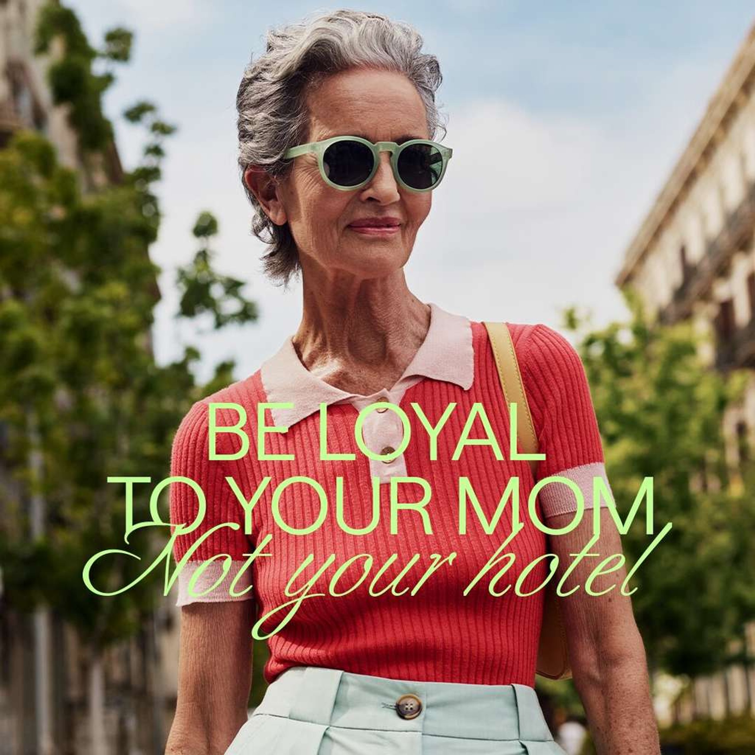 Stylish older woman in coral knit top and green sunglasses with Be Loyal To Your Mom text for Hoxton Hotel