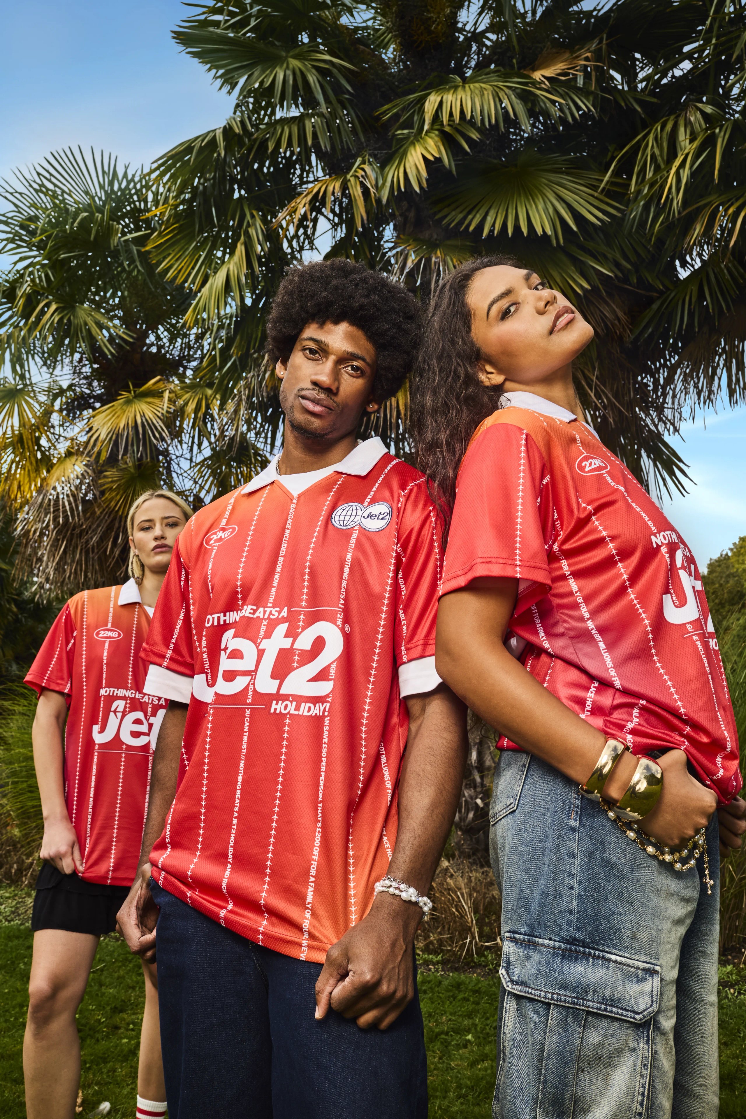 Two models in red Jet2 football jerseys standing under palm tree with third model behind