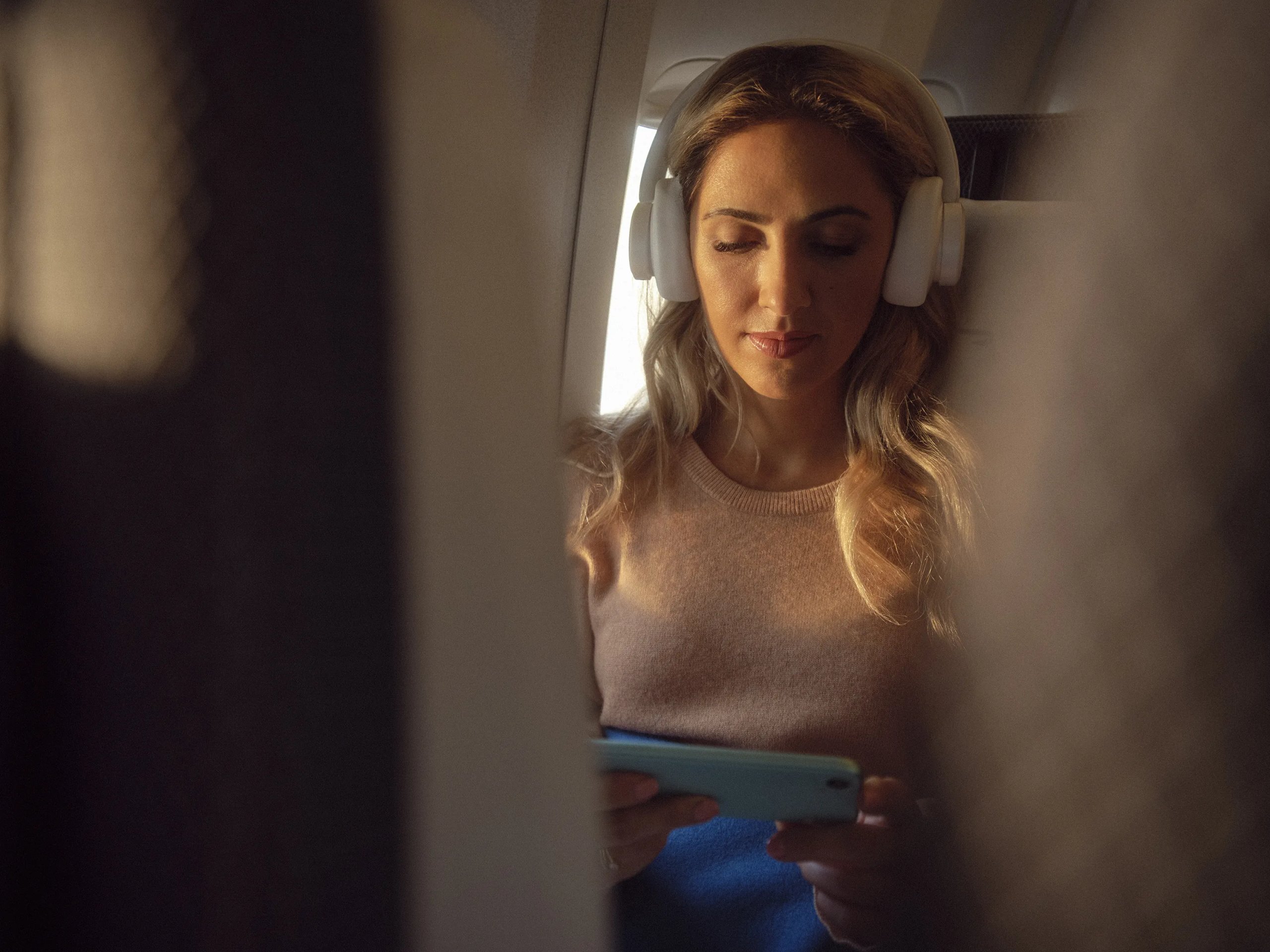 Woman wearing headphones browsing tablet in British Airways premium economy seat by window