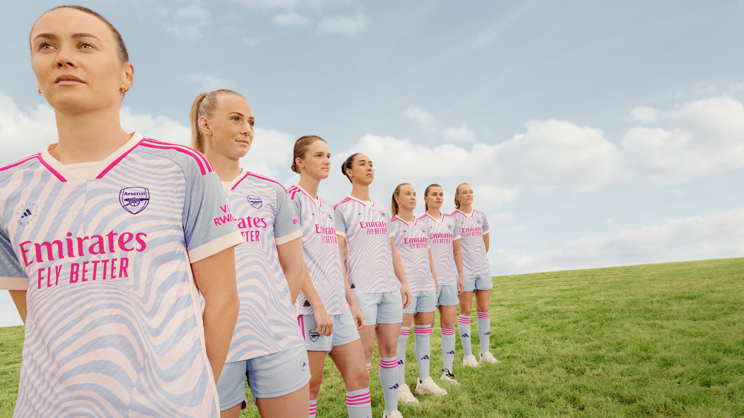 Arsenal Women squad lined up on green pitch in Stella McCartney pastel wave-print away kit