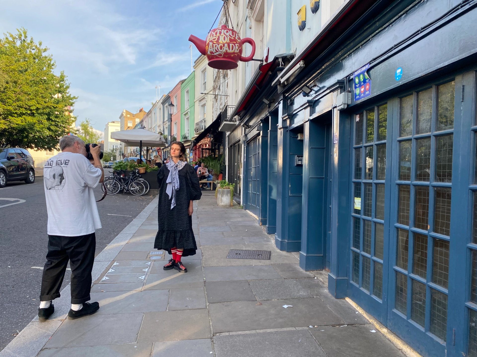 Photographer shooting model in black maxi dress outside Portobello Road antiques arcade with red teapot sign