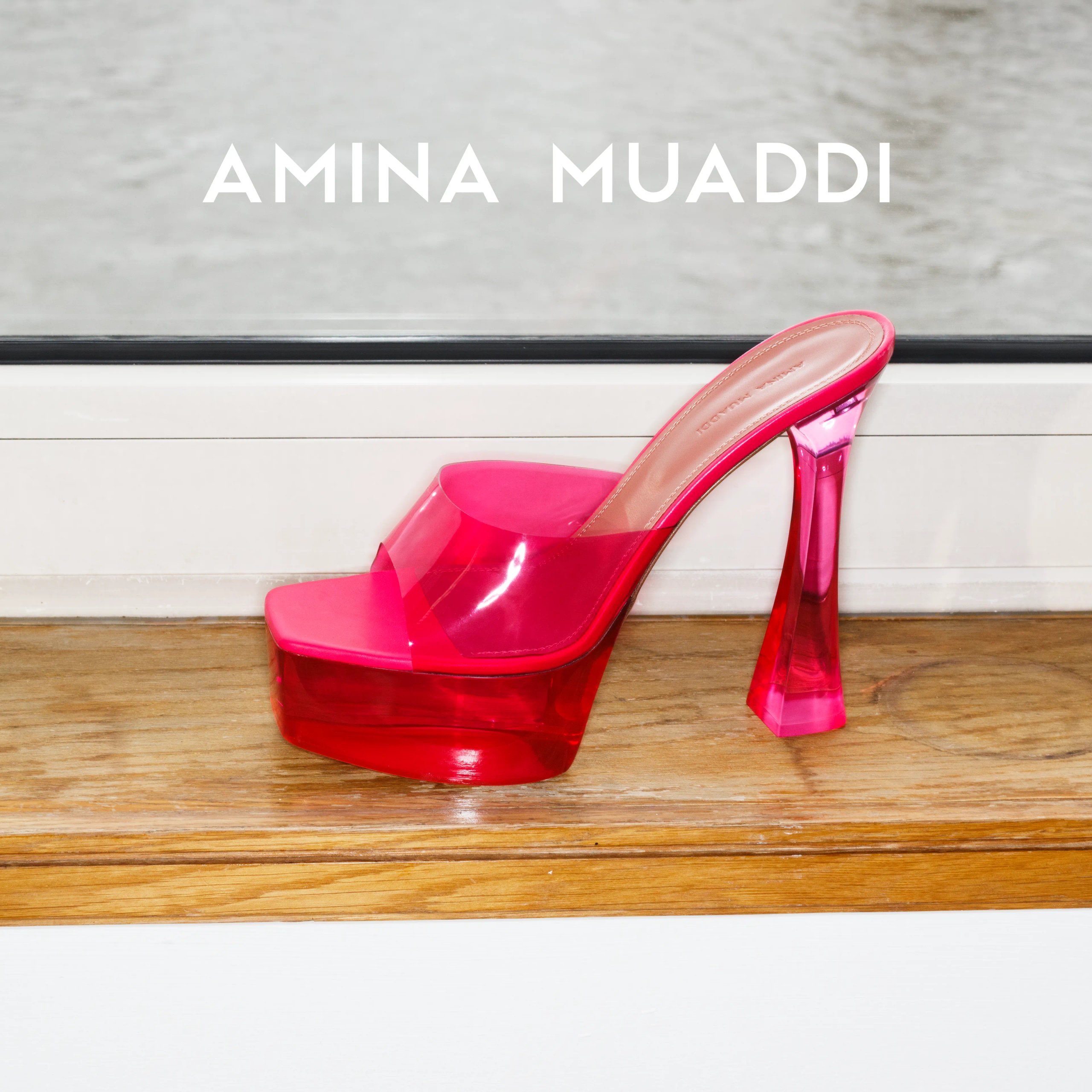 Amina Muaddi hot pink transparent platform mule on wooden windowsill