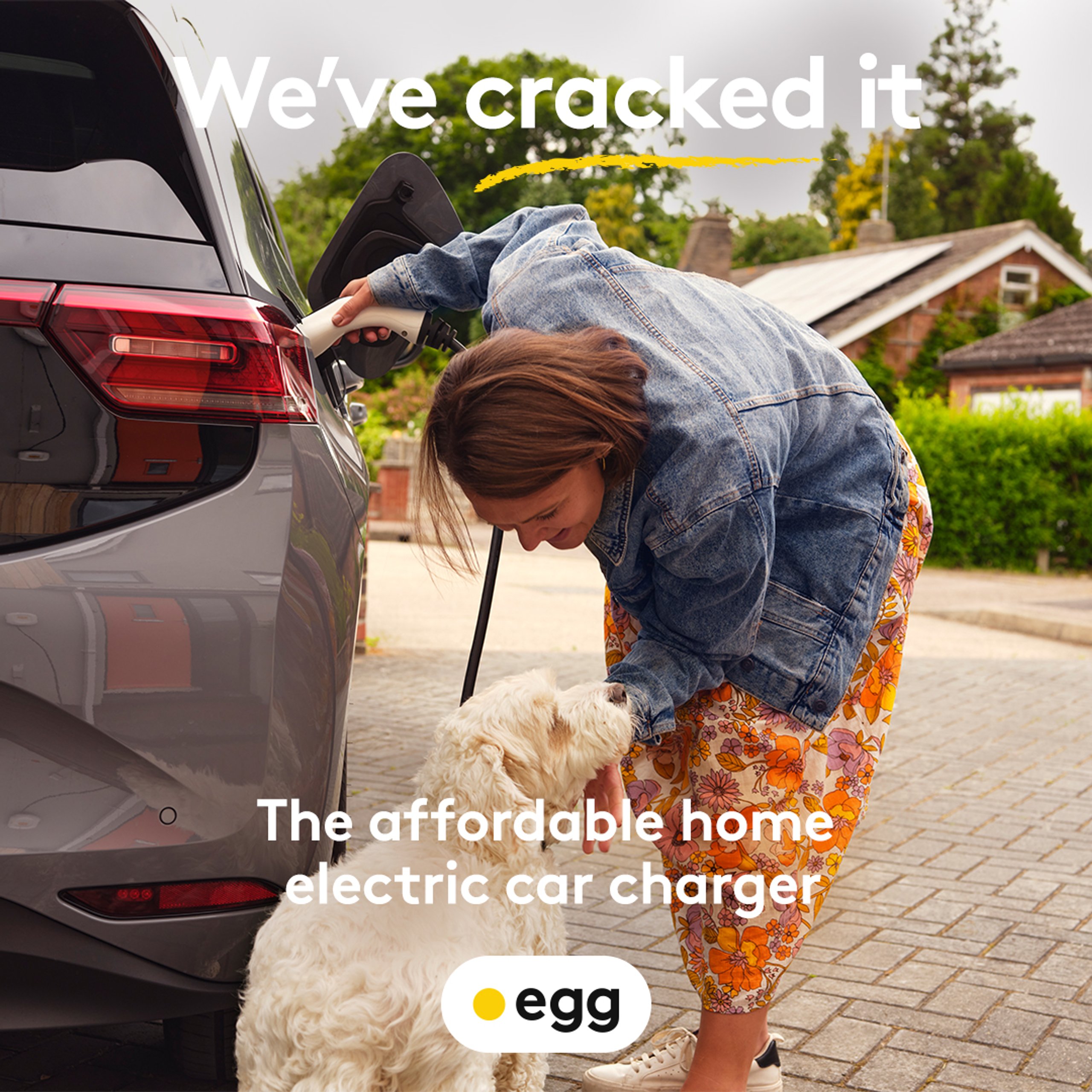 Woman plugging in EGG home electric car charger while petting dog on driveway for Cracked It campaign