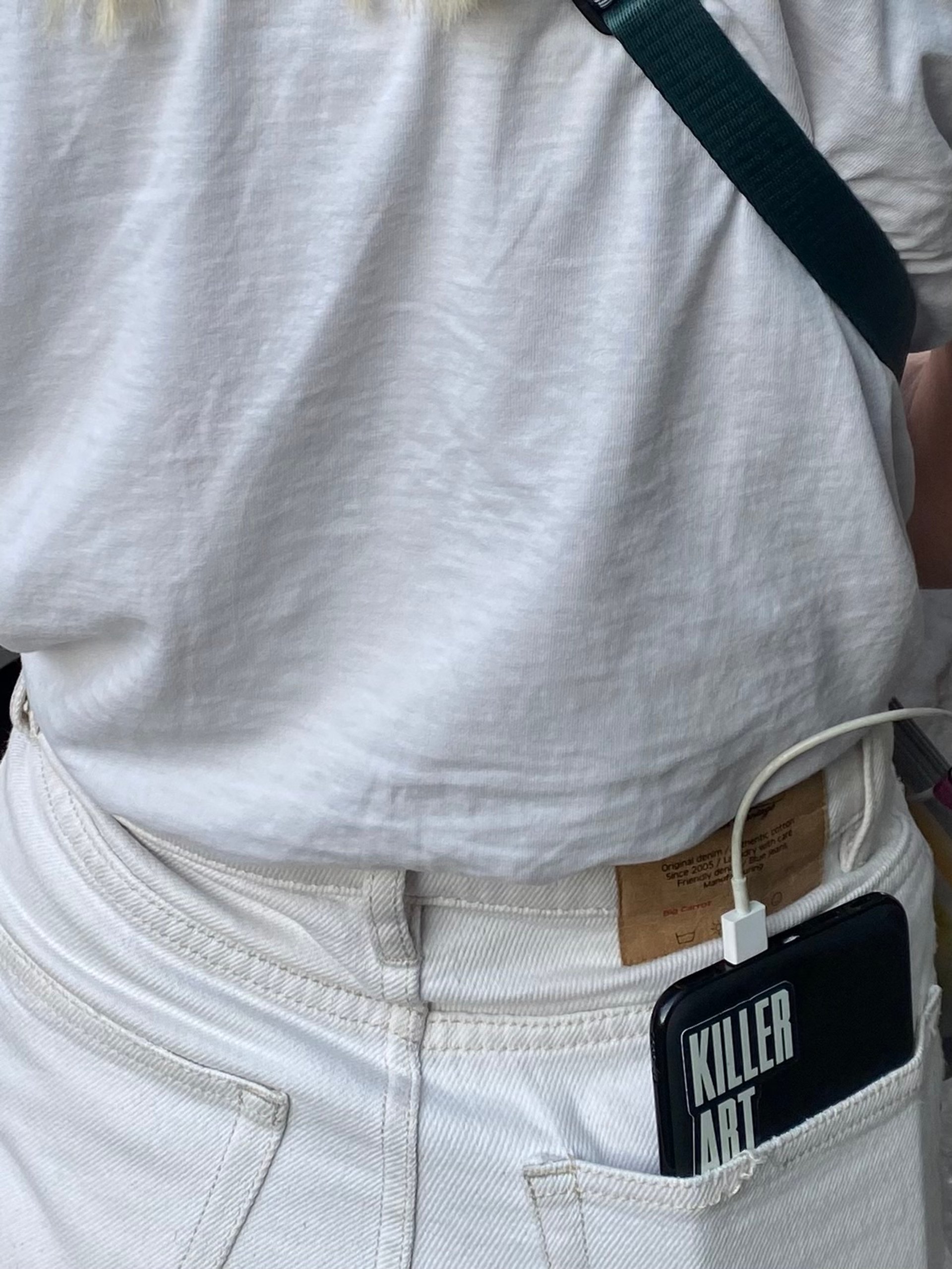 Close-up of KILLER Art phone case in back pocket of white jeans with camera strap over white tee