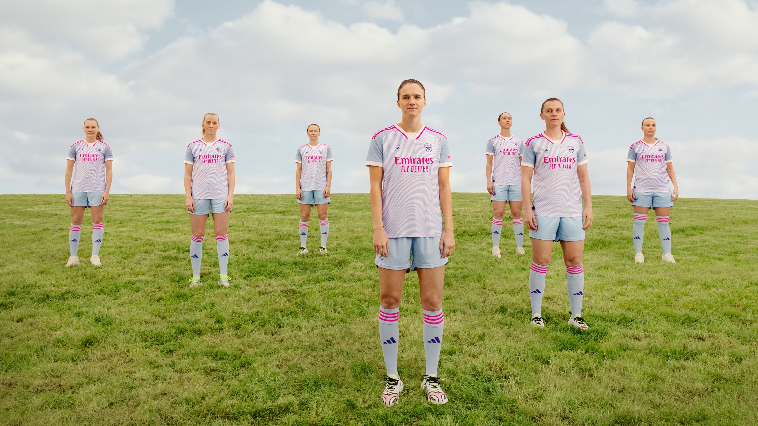 Arsenal Women squad standing in formation on green pitch in full Stella McCartney away kit with pink socks
