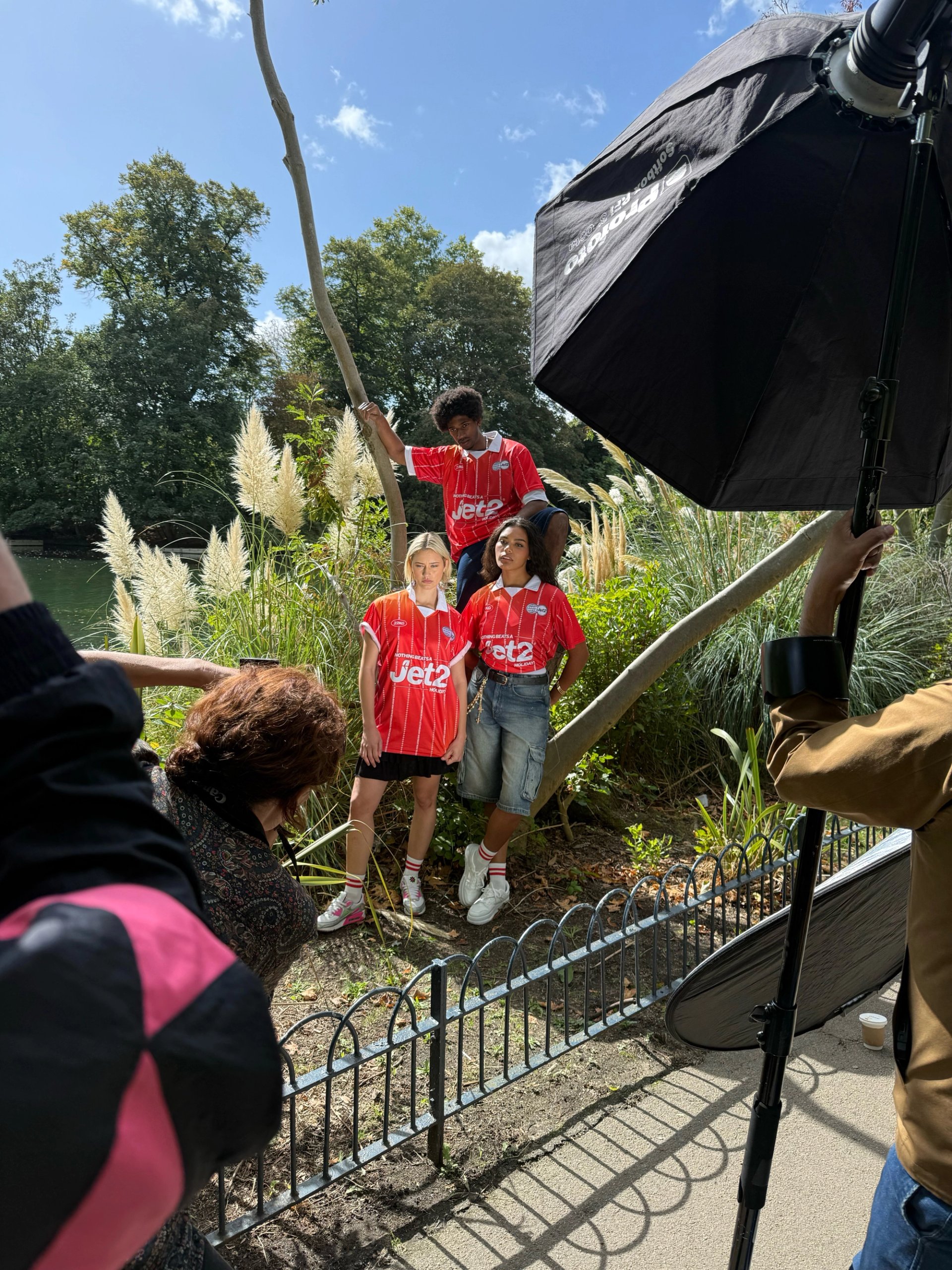 Behind the scenes of Jet2 shoot with crew photographing three models in red jerseys among pampas grass by lake