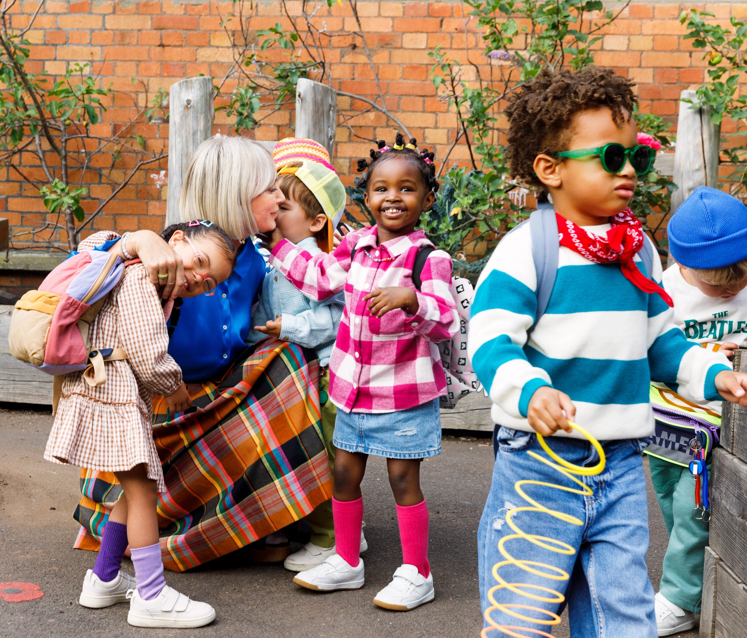 Nursery school drop-off with children in colourful outfits and teacher kissing child goodbye