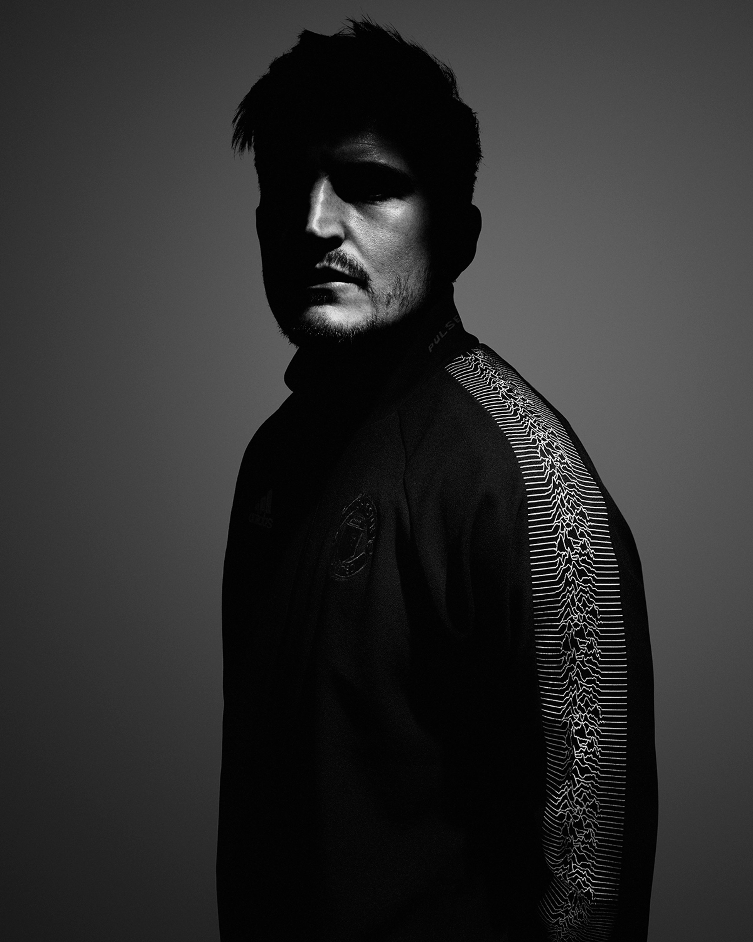 Black and white portrait in Peter Saville track jacket with Joy Division Unknown Pleasures waveform sleeve detail