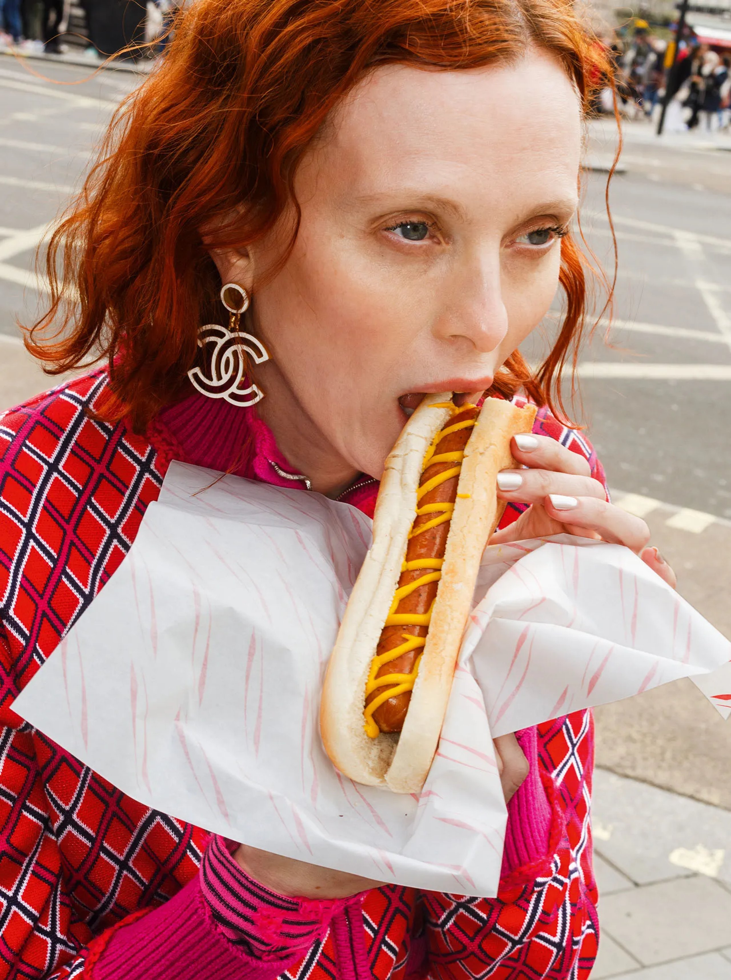 Karen Elson eating hot dog in Chanel red diamond-print tracksuit with CC earrings on London street