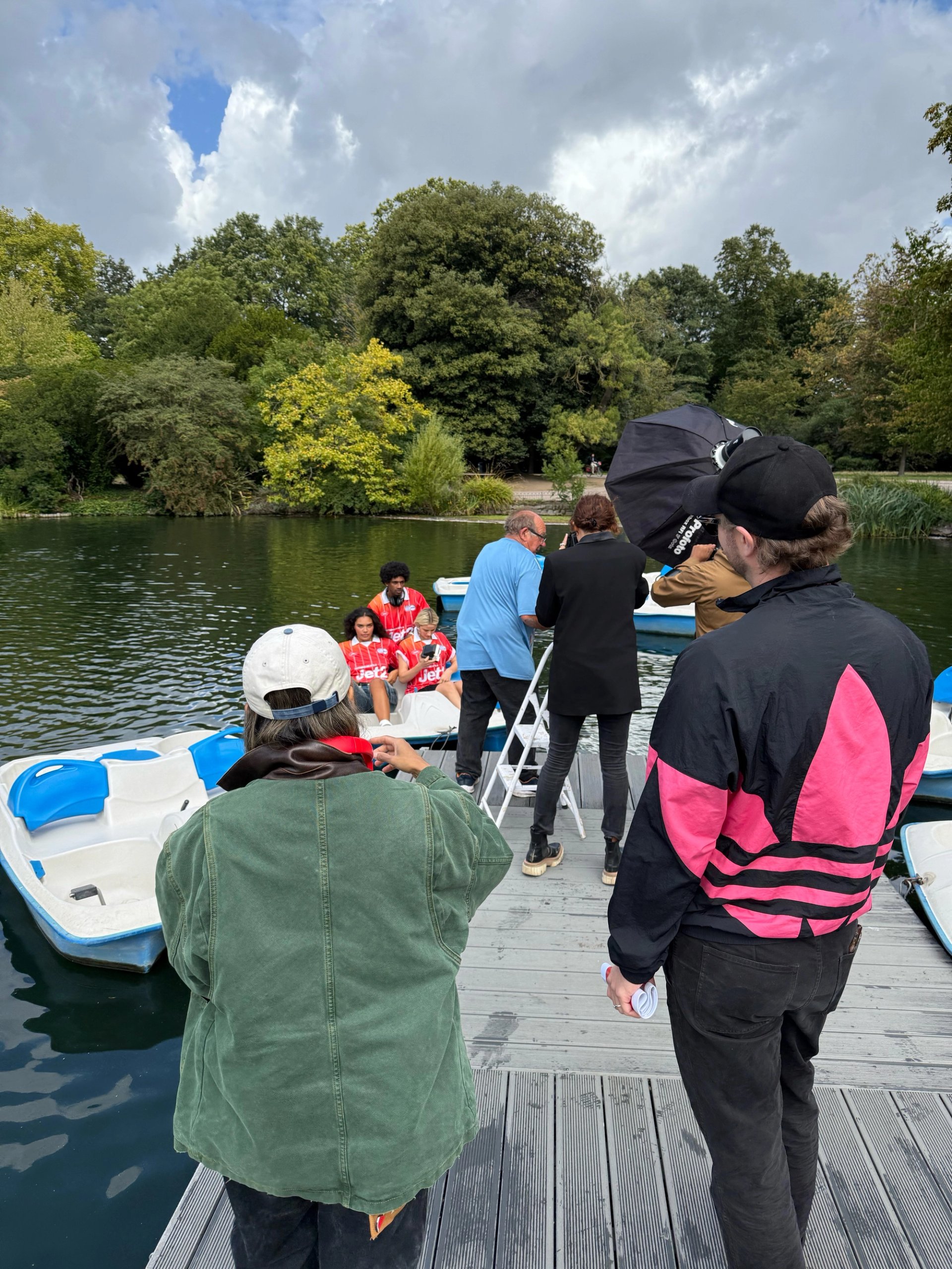 Production crew on lake jetty directing models in red Jet2 jerseys seated in pedal boat with softbox and reflector
