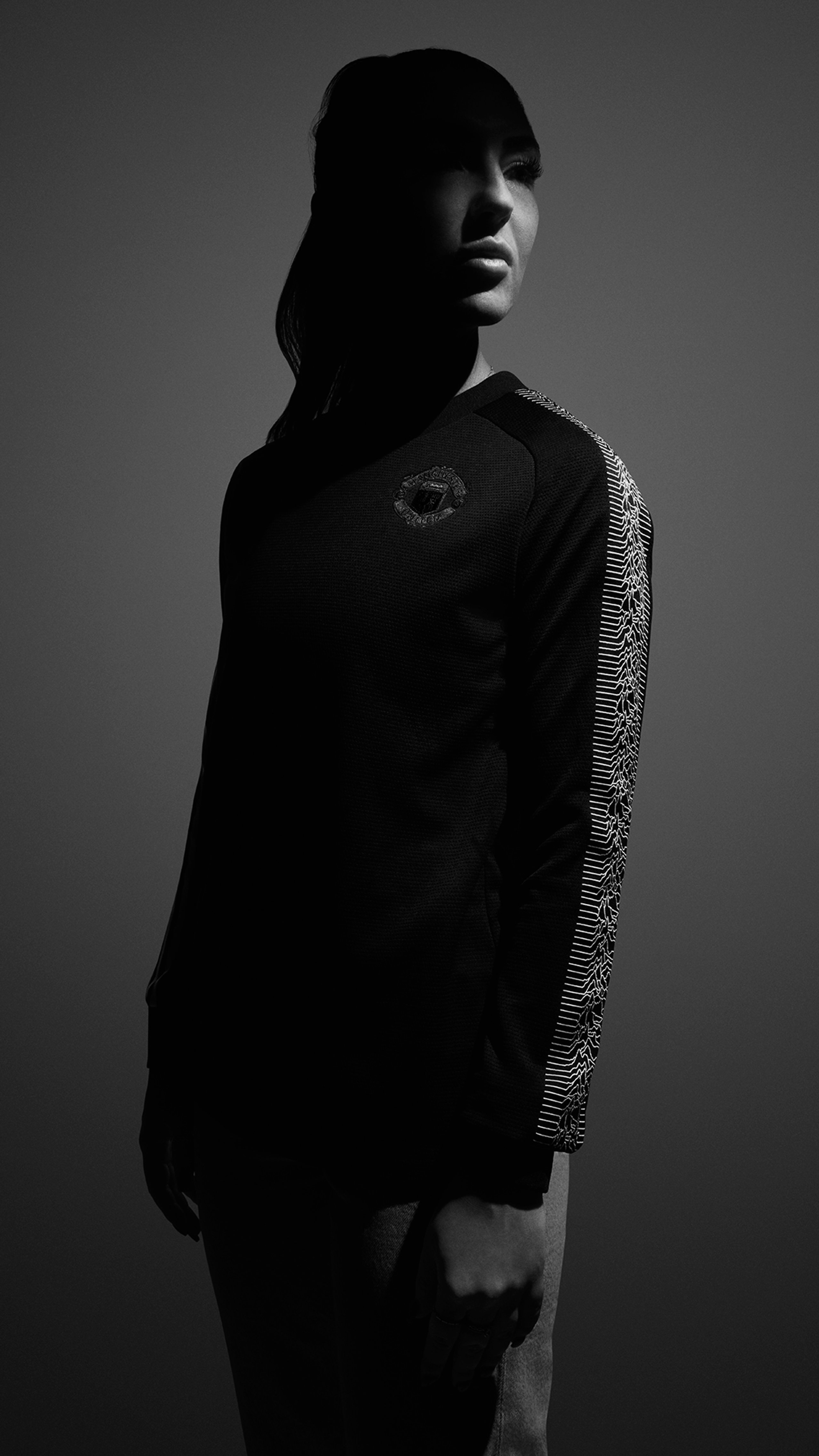 Black and white portrait of woman in Peter Saville x Manchester United track top with Joy Division waveform sleeve
