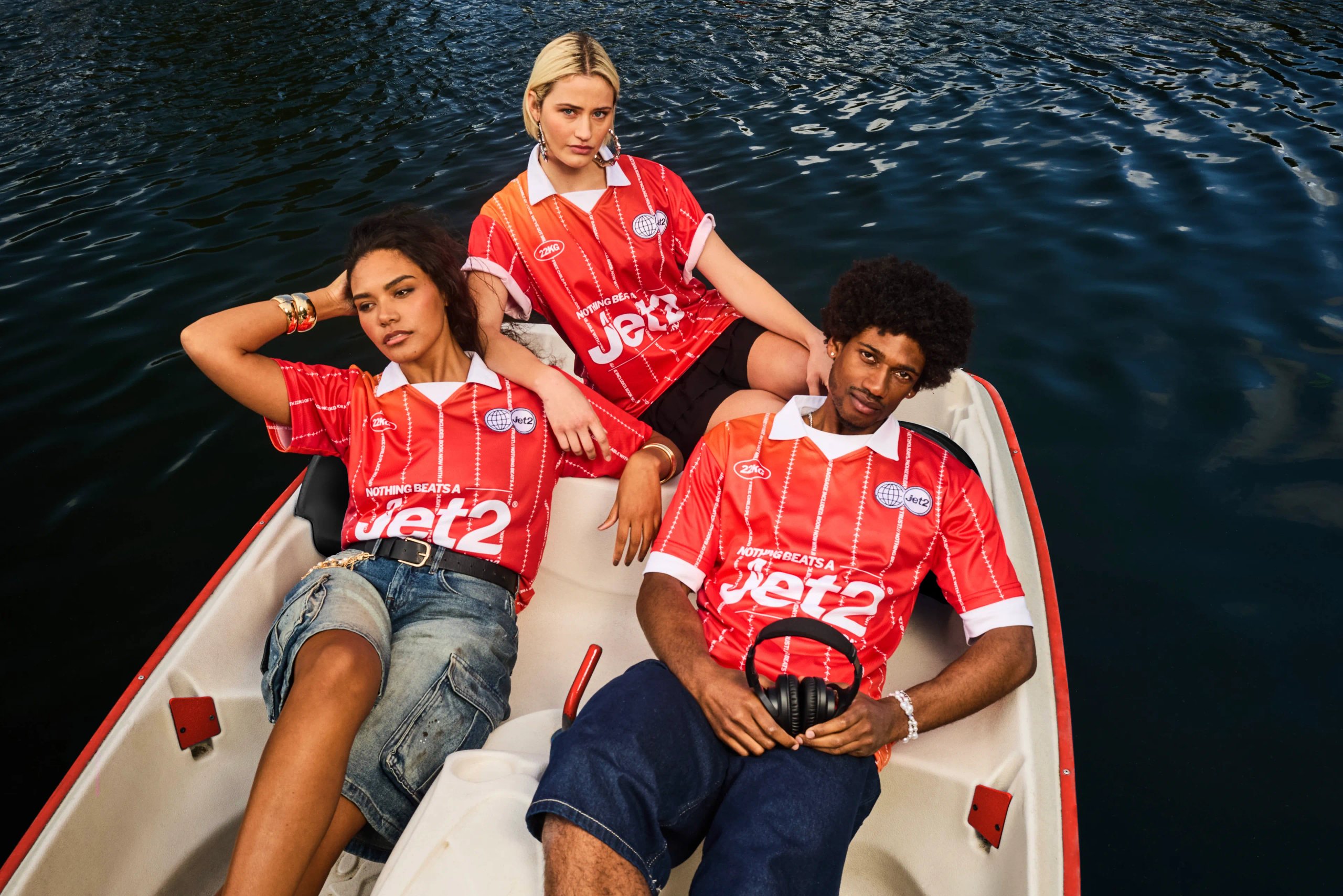 Three models in red Jet2 football jerseys posing in white rowing boat on lake