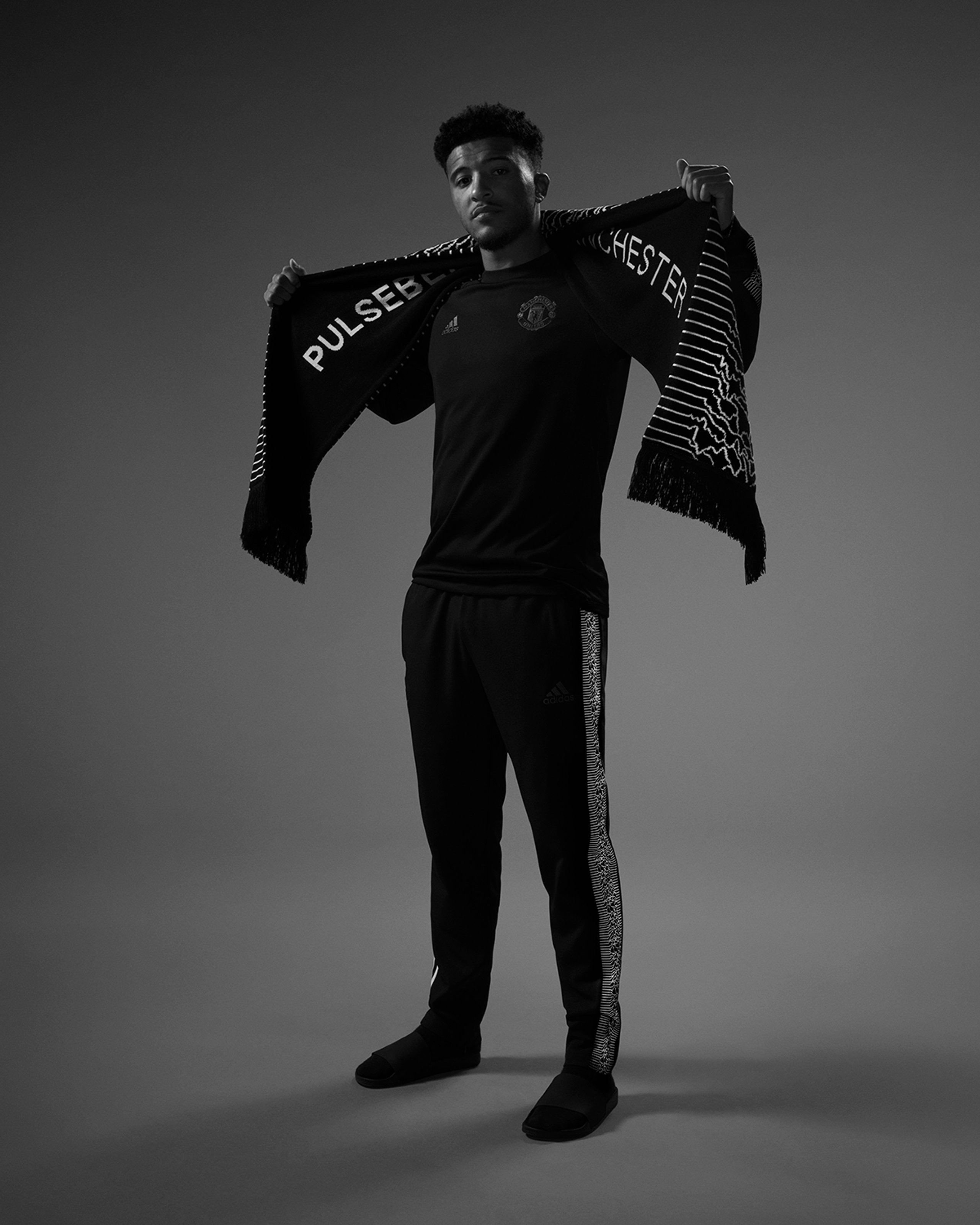 Jadon Sancho displaying Pulsebeat Manchester scarf in black and white portrait wearing Peter Saville collection