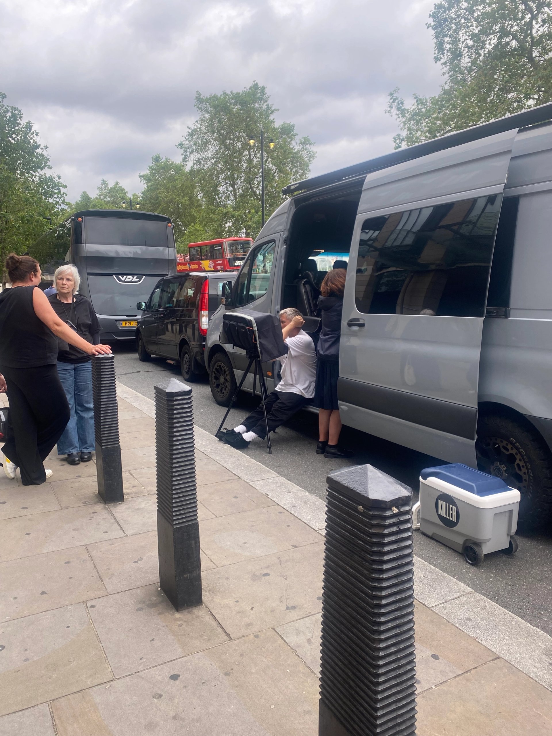 Production crew loading silver van on London street with KILLER cooler box and red bus in background