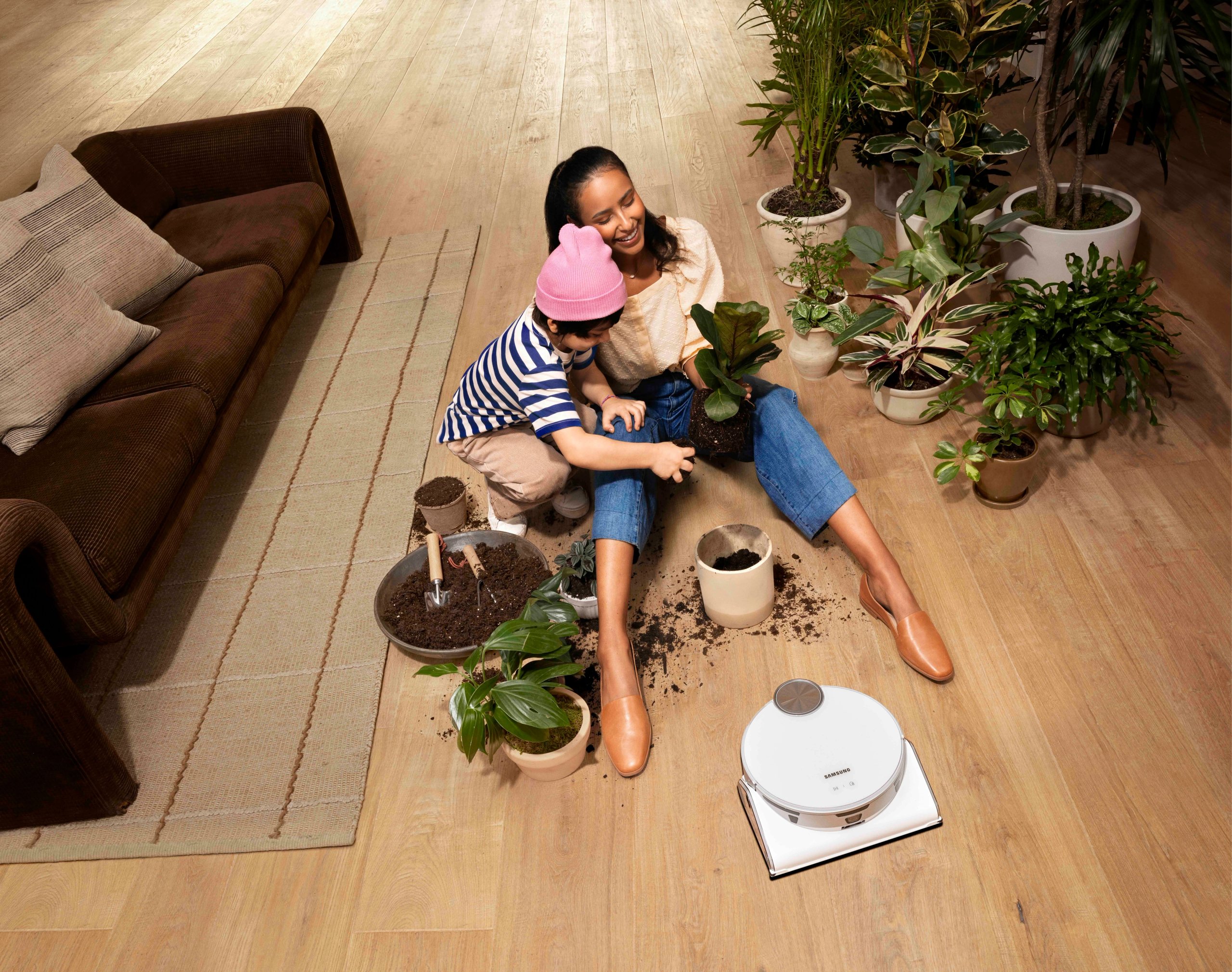 Mother and child potting plants on living room floor with Samsung Jet Bot robot vacuum
