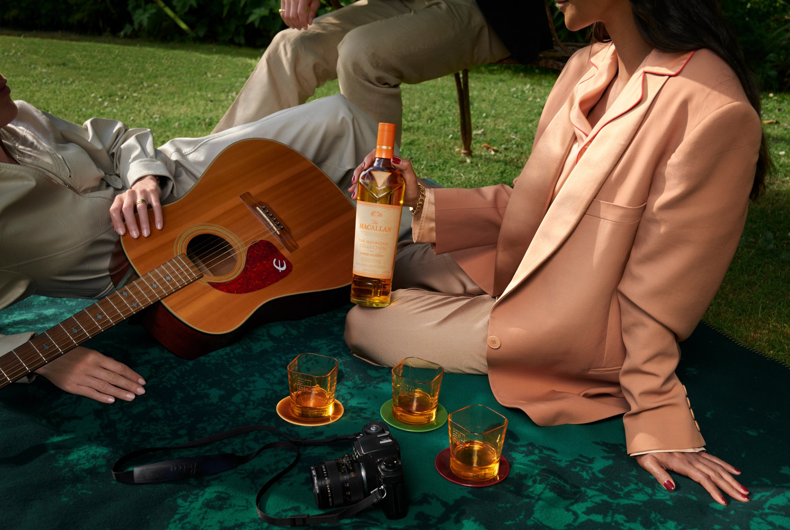 Couple on garden blanket with Macallan Harmony Collection bottle, acoustic guitar and whisky glasses