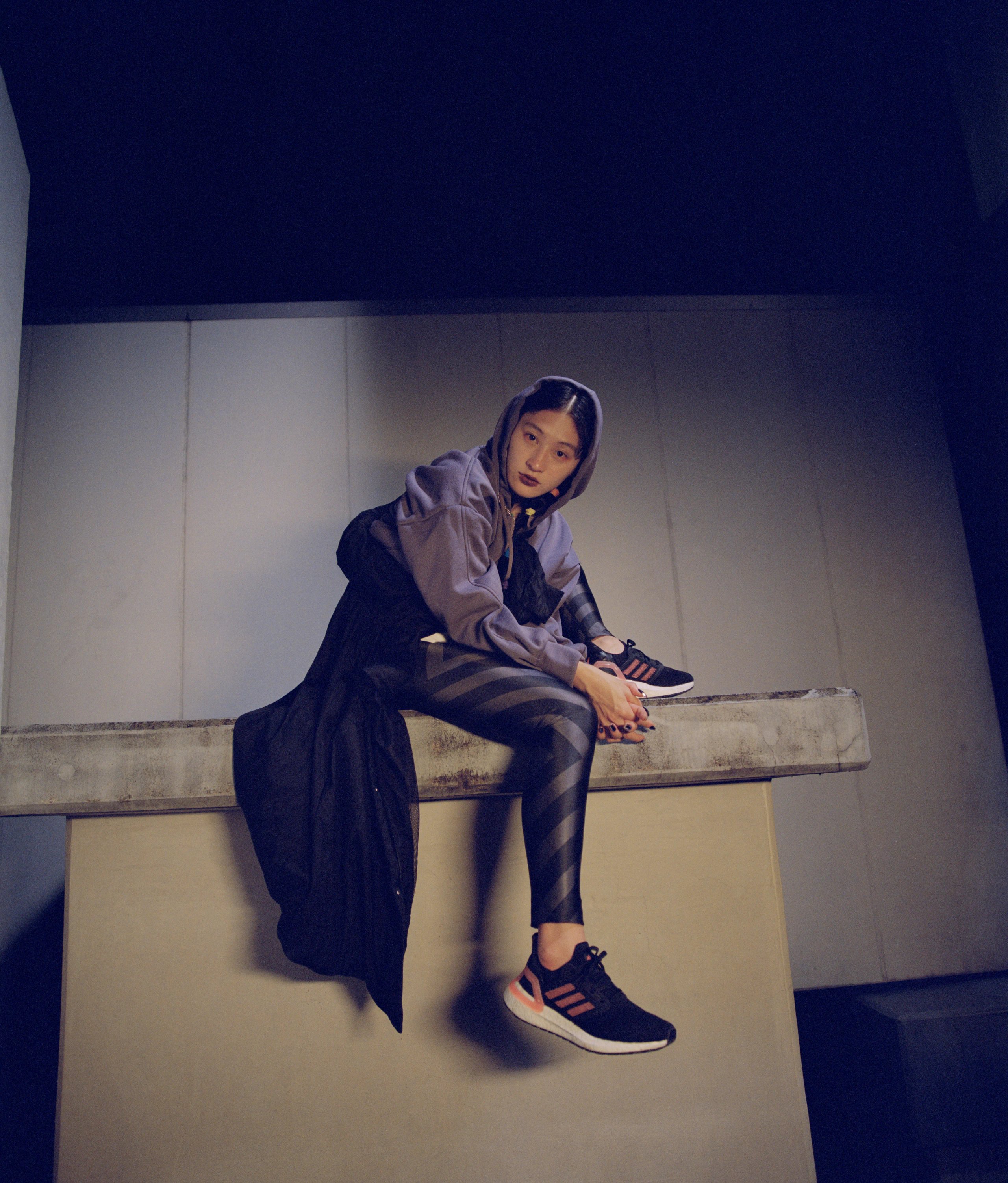 Athlete seated on concrete ledge in purple adidas hoodie and striped leggings with Ultraboost trainers at night