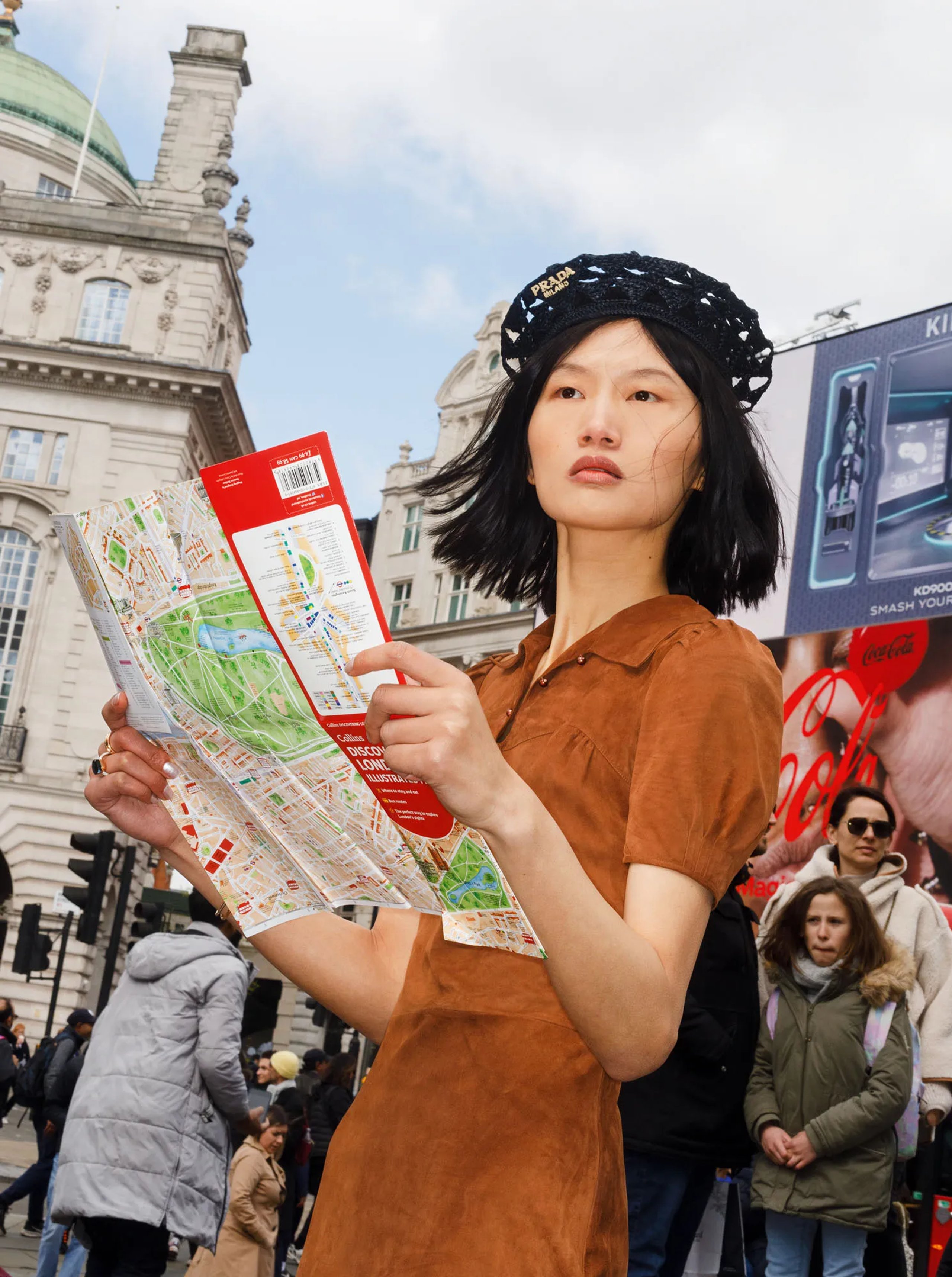Model in Prada beret and brown suede dress reading London map at Piccadilly Circus
