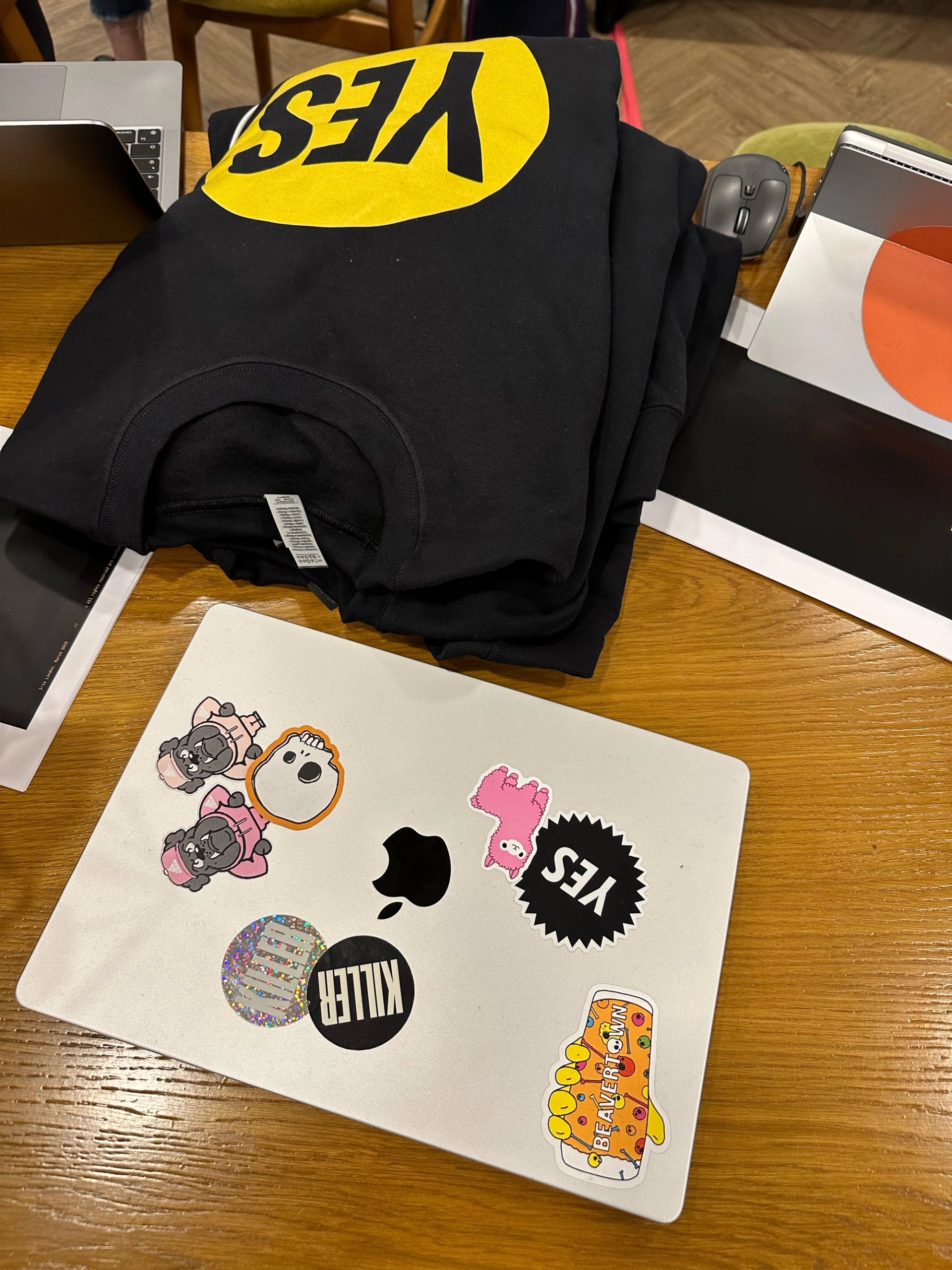 YES! charity branded black hoodie on desk with MacBook covered in KILLER and YES! stickers