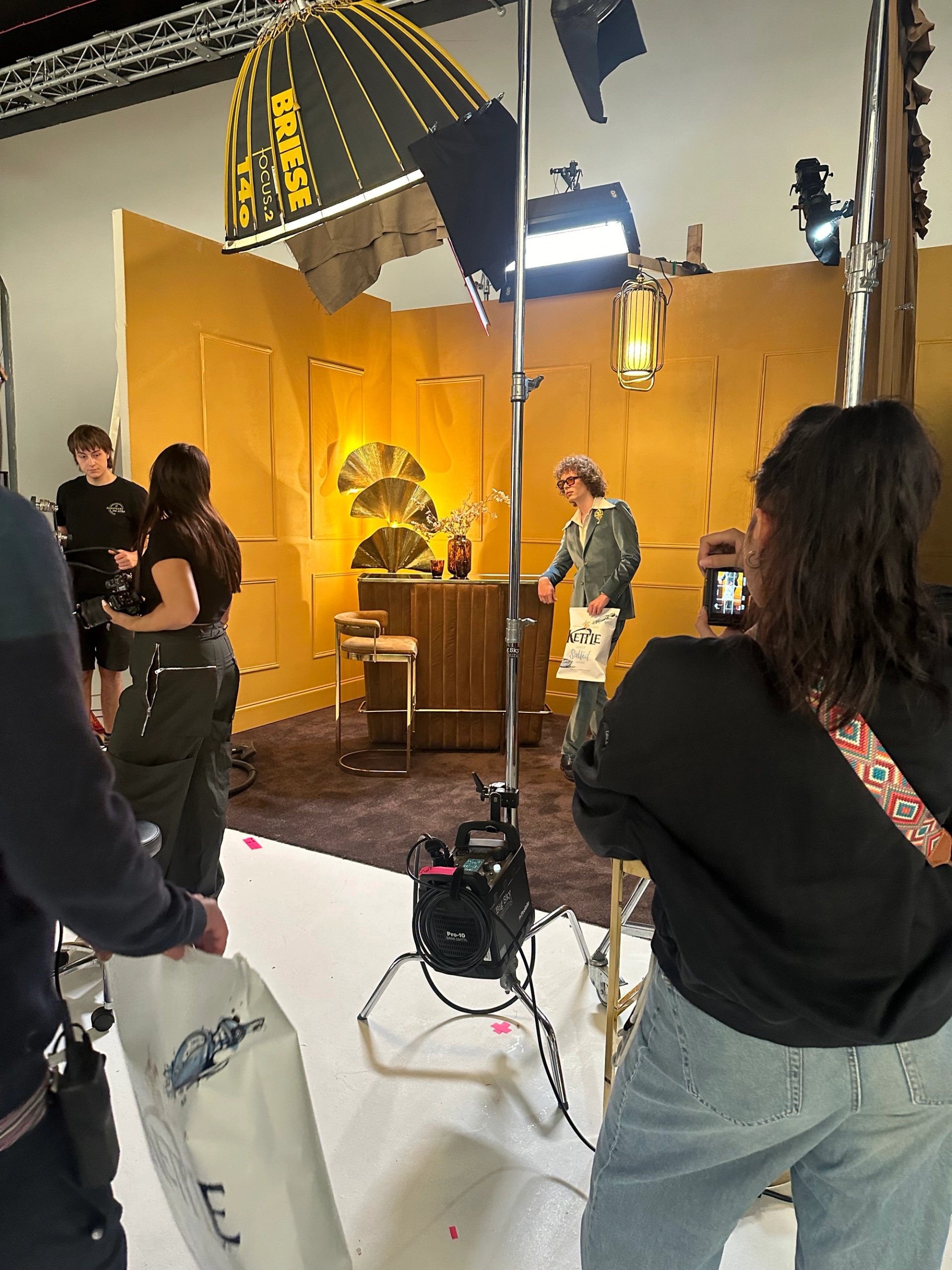Behind the scenes on KETTLE Chips set with crew and Briese lighting on mustard panelled backdrop with gold fan props