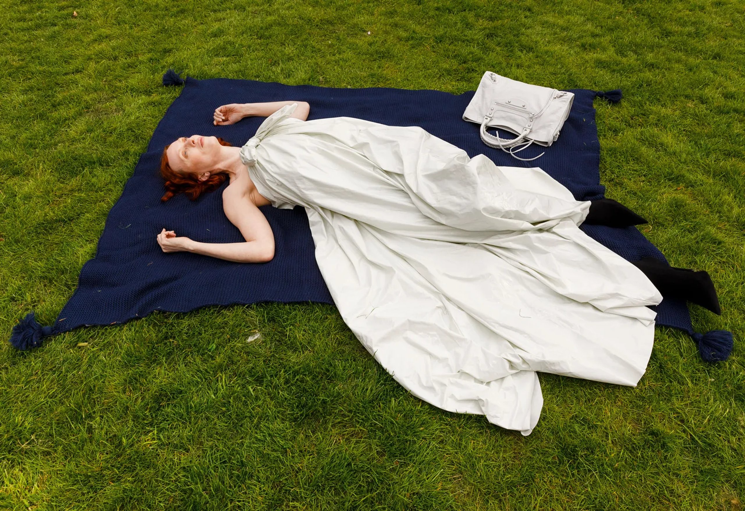 Karen Elson lying on navy blanket in flowing white gown on green park lawn