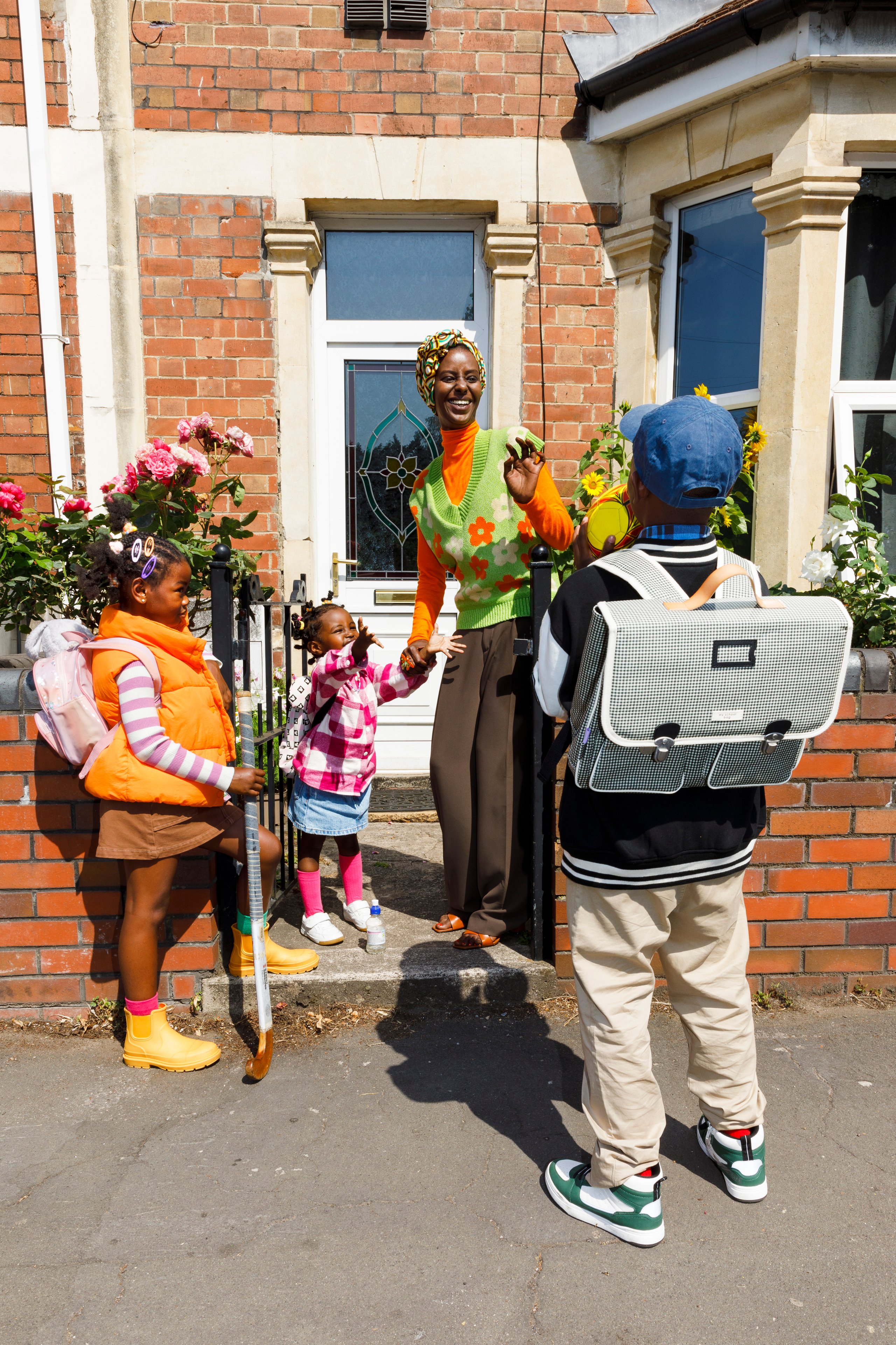 Mother greeting children at front door on school run morning with colourful backpacks and yellow wellies