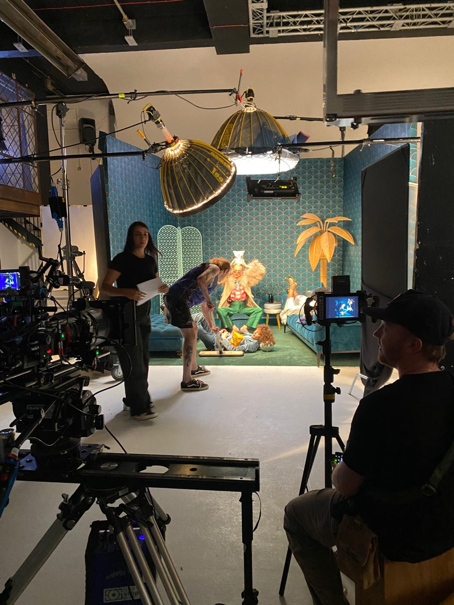 Behind the scenes on KETTLE set with crew directing talent on teal art deco set with palm tree prop and Briese lights