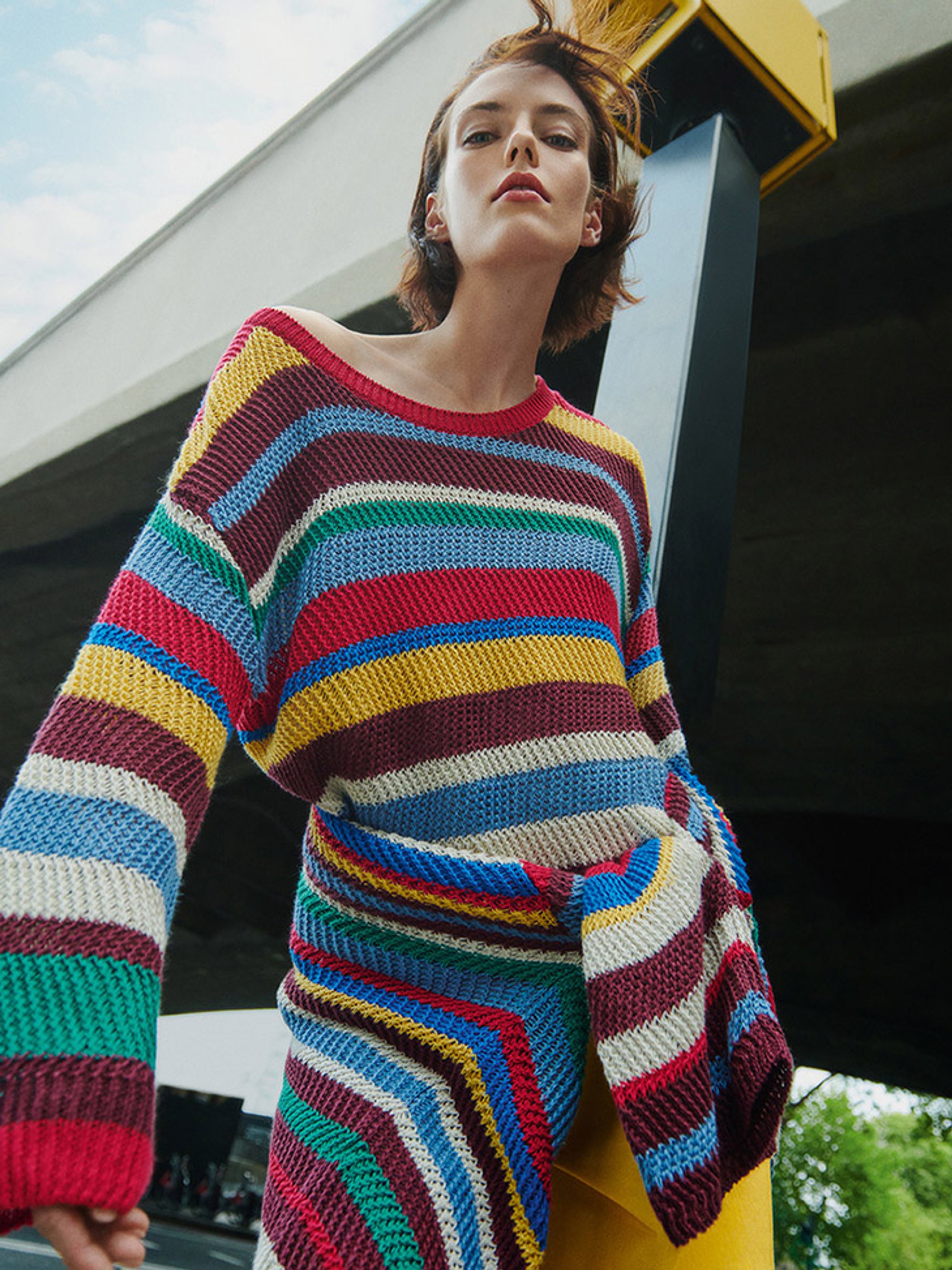 Model in multicolour striped crochet knit dress shot from below against urban overpass