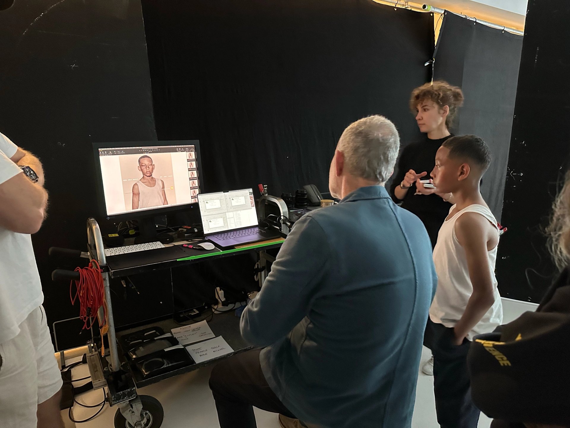 Behind the scenes of YES! shoot with young boy reviewing portrait on tethered monitor with photographer and makeup artist