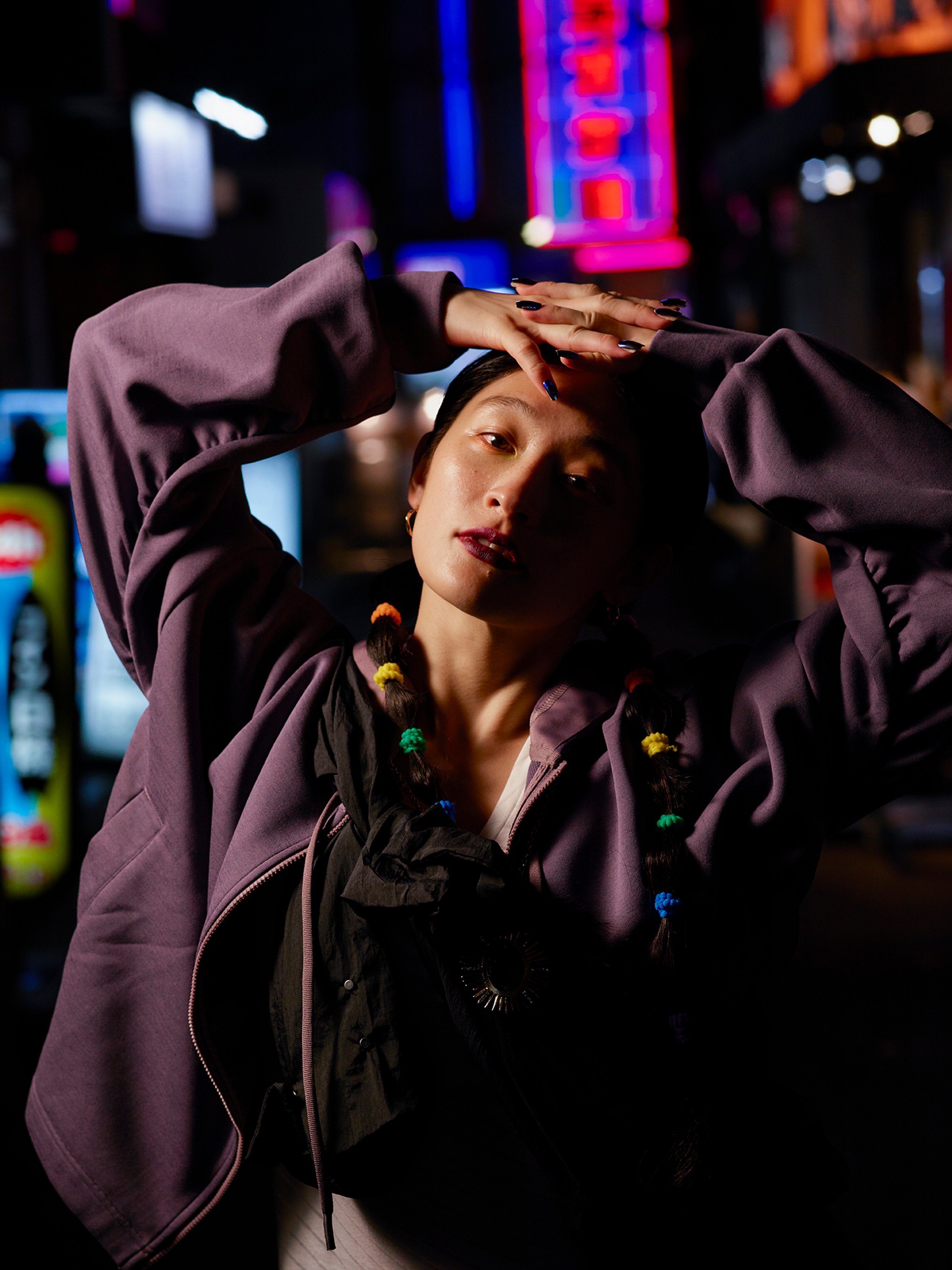 Athlete in purple adidas hoodie with colourful braids posing under Tokyo neon lights at night
