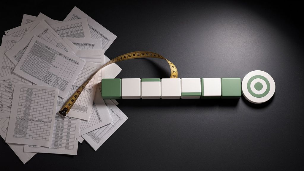 Composición de escritorio: papeles con cuadrículas desordenados a la izquierda, sistema modular ordenado a la derecha, cinta métrica y un objetivo al fondo.