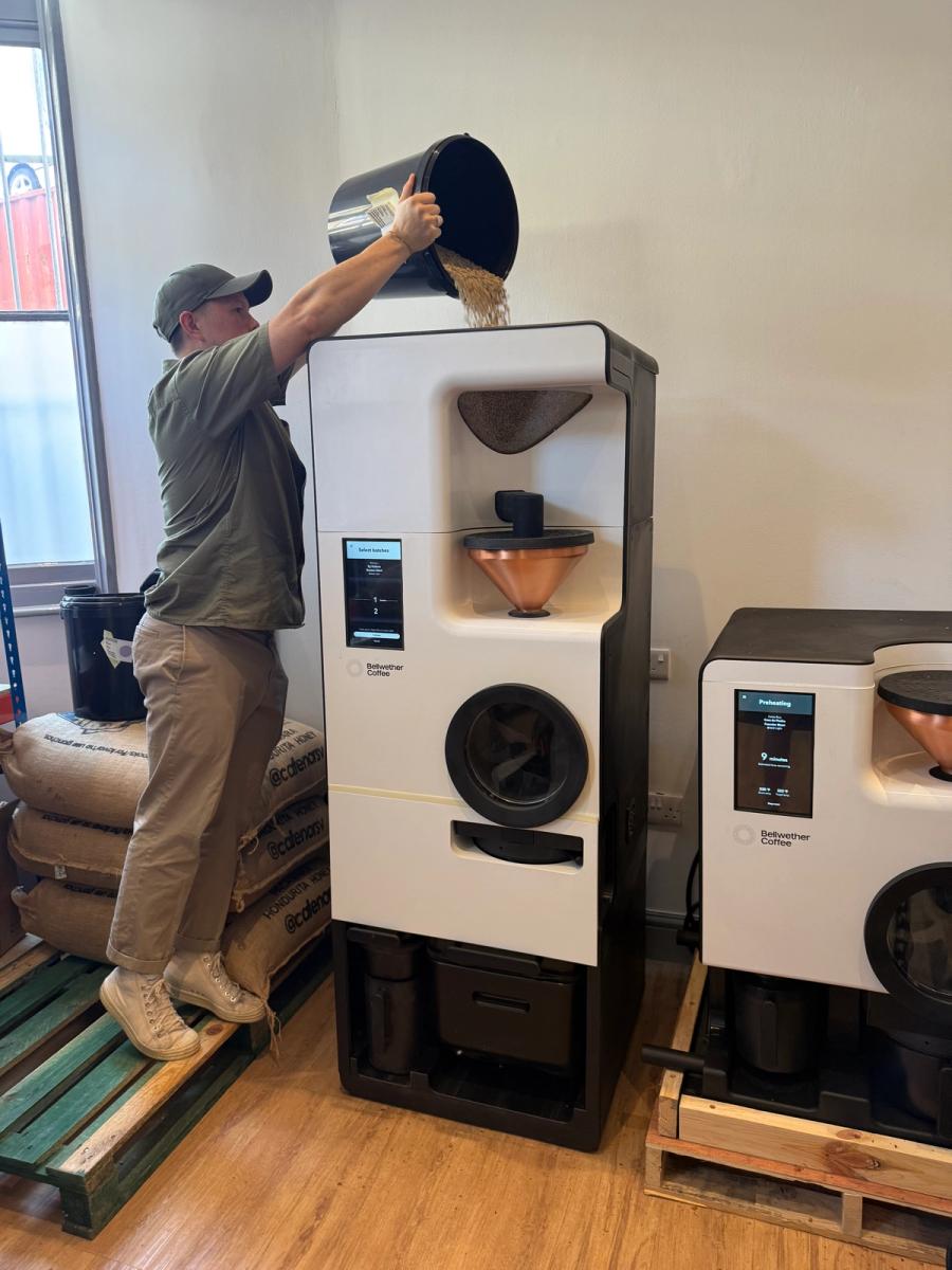A High Grade Coffee barista pours green beans into the Bellwether Shop Roaster at their London roastery, with a second Shop Roaster preheating alongside.