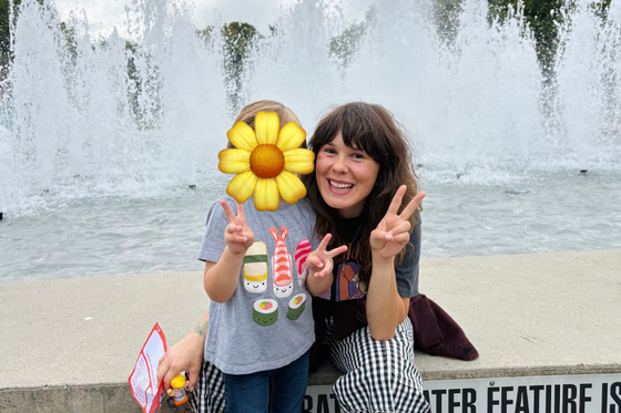 Cayley and a child making peace signs in front of a fountain on an overcast day.
