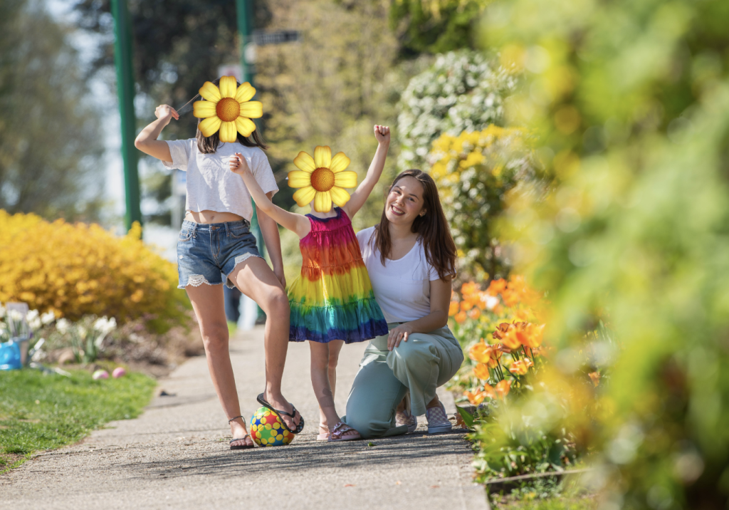 Cayley crouching on a garden path in spring, cheering with two children among the flower beds.